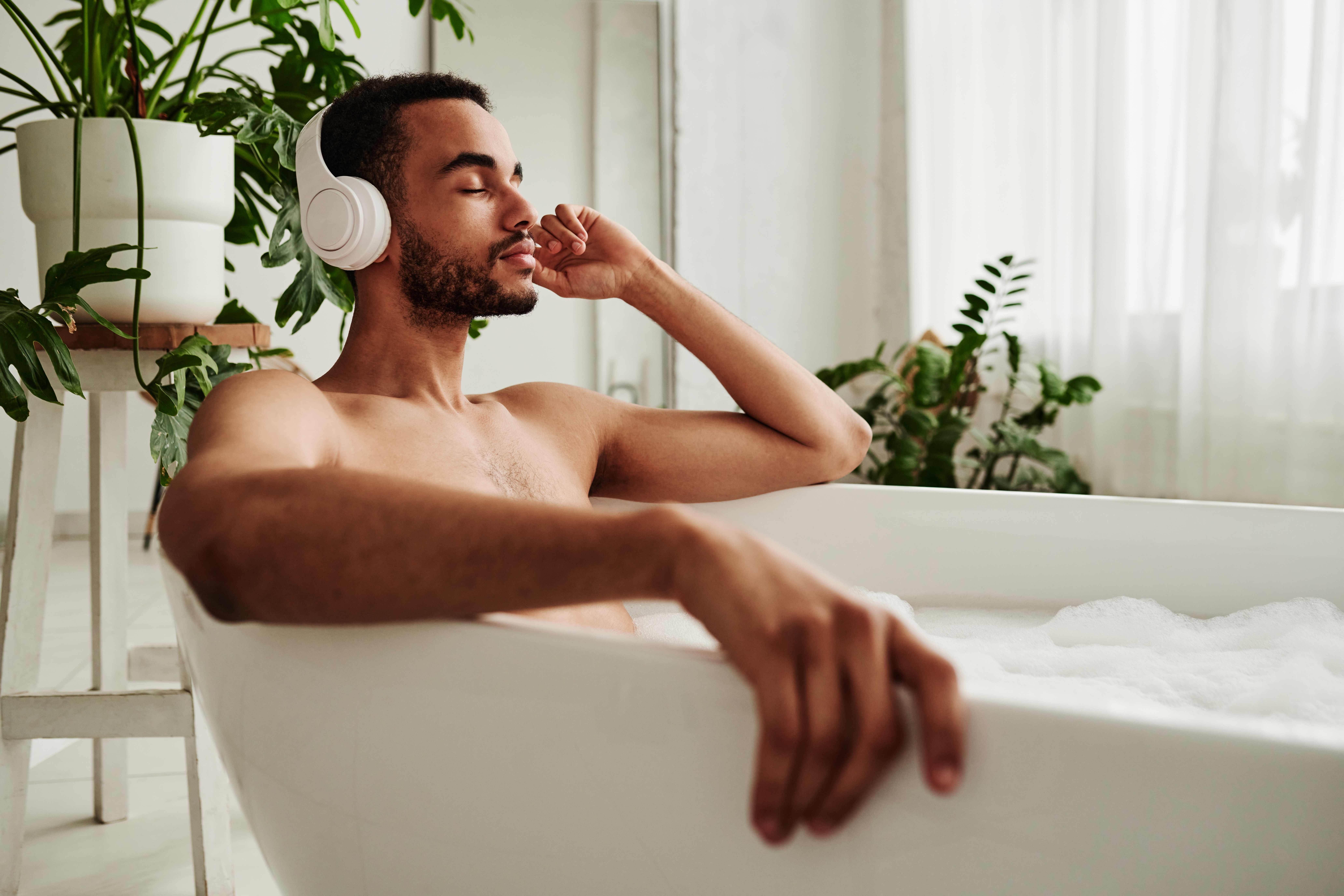 A Taurus man practices self-care by taking a bubble bath and listening to music.