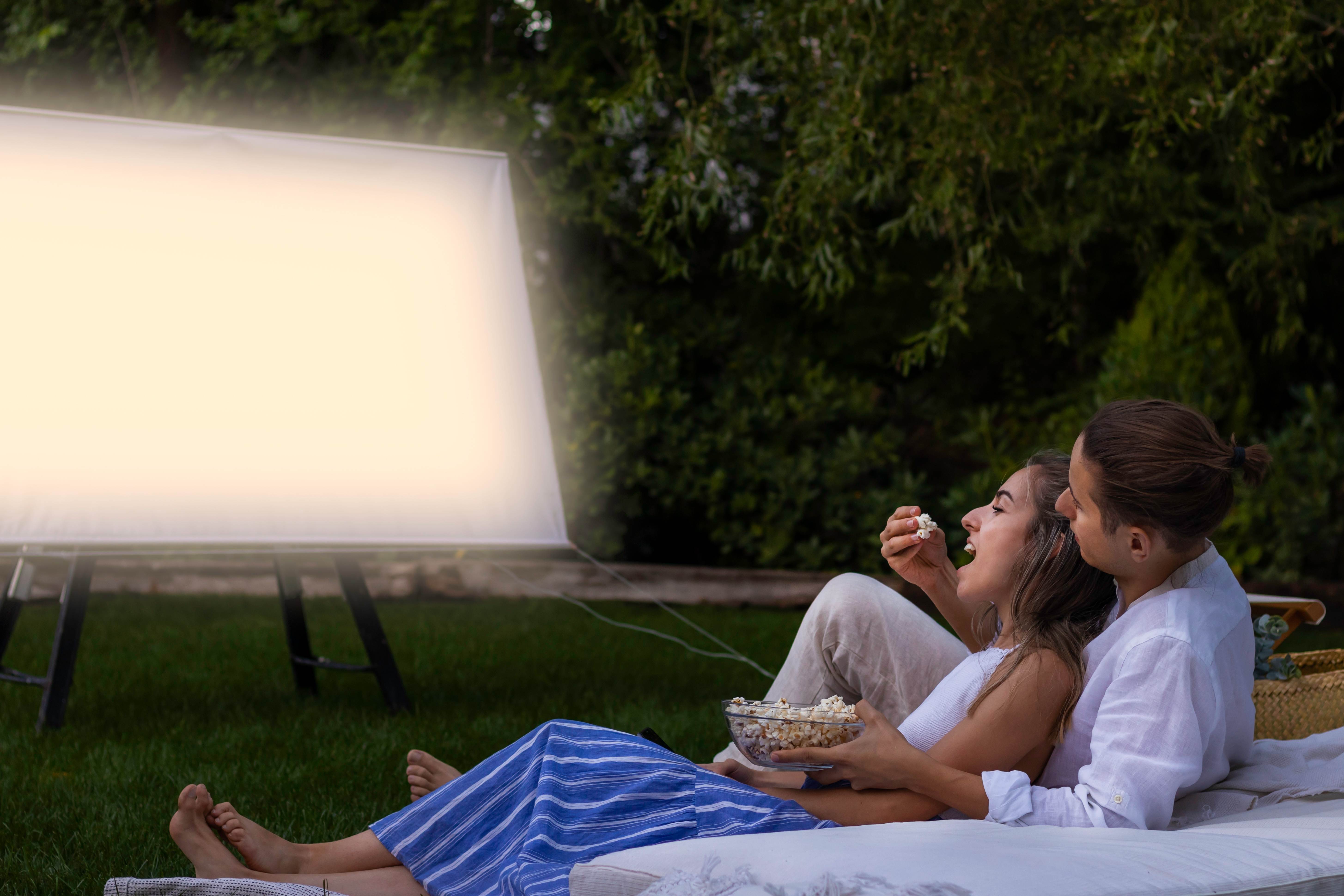 A loving couple watches an outdoor movie together on a summer night
