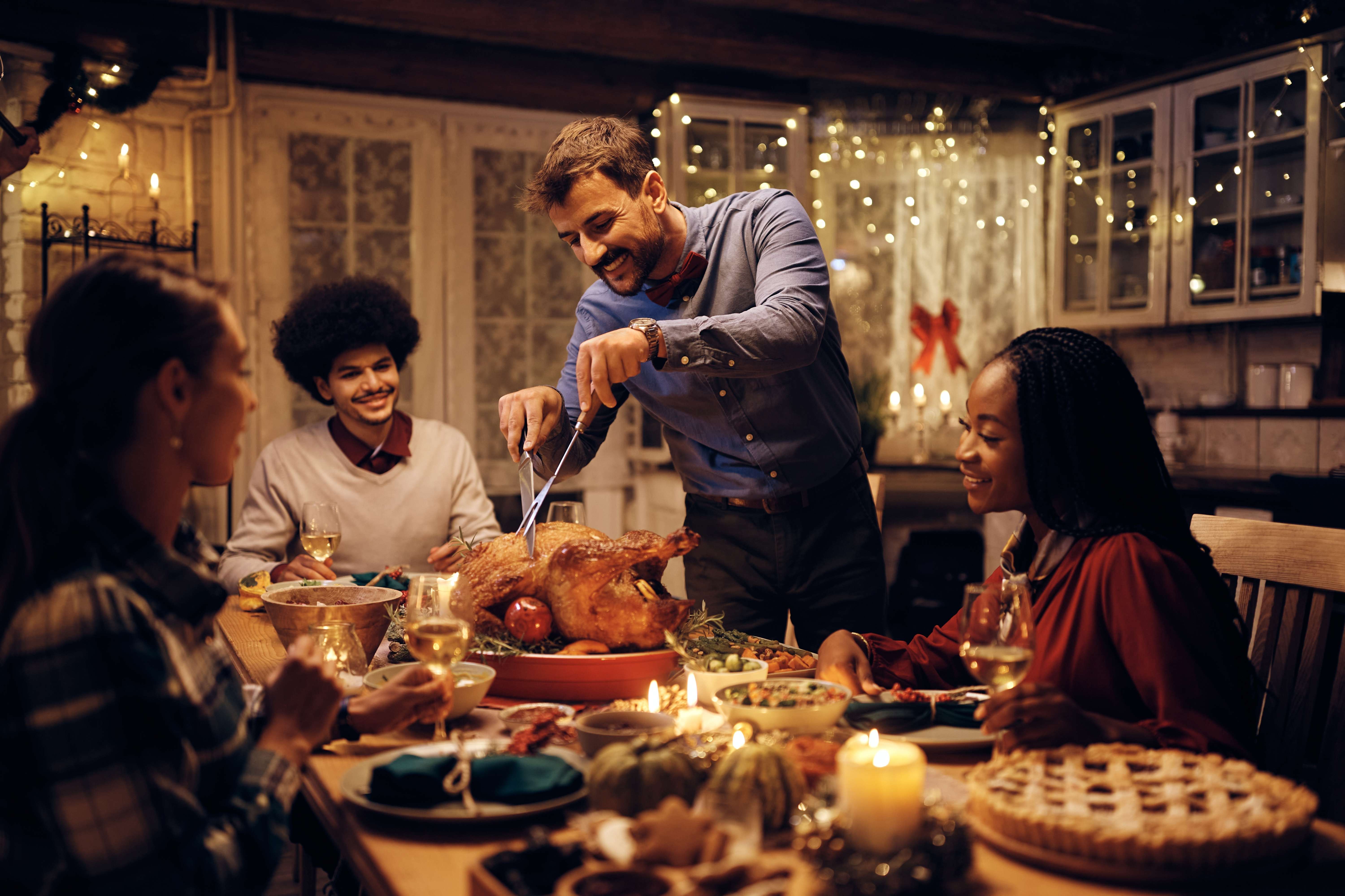 A thoughtful host carves the Thanksgiving turkey for his family at the dinner table.