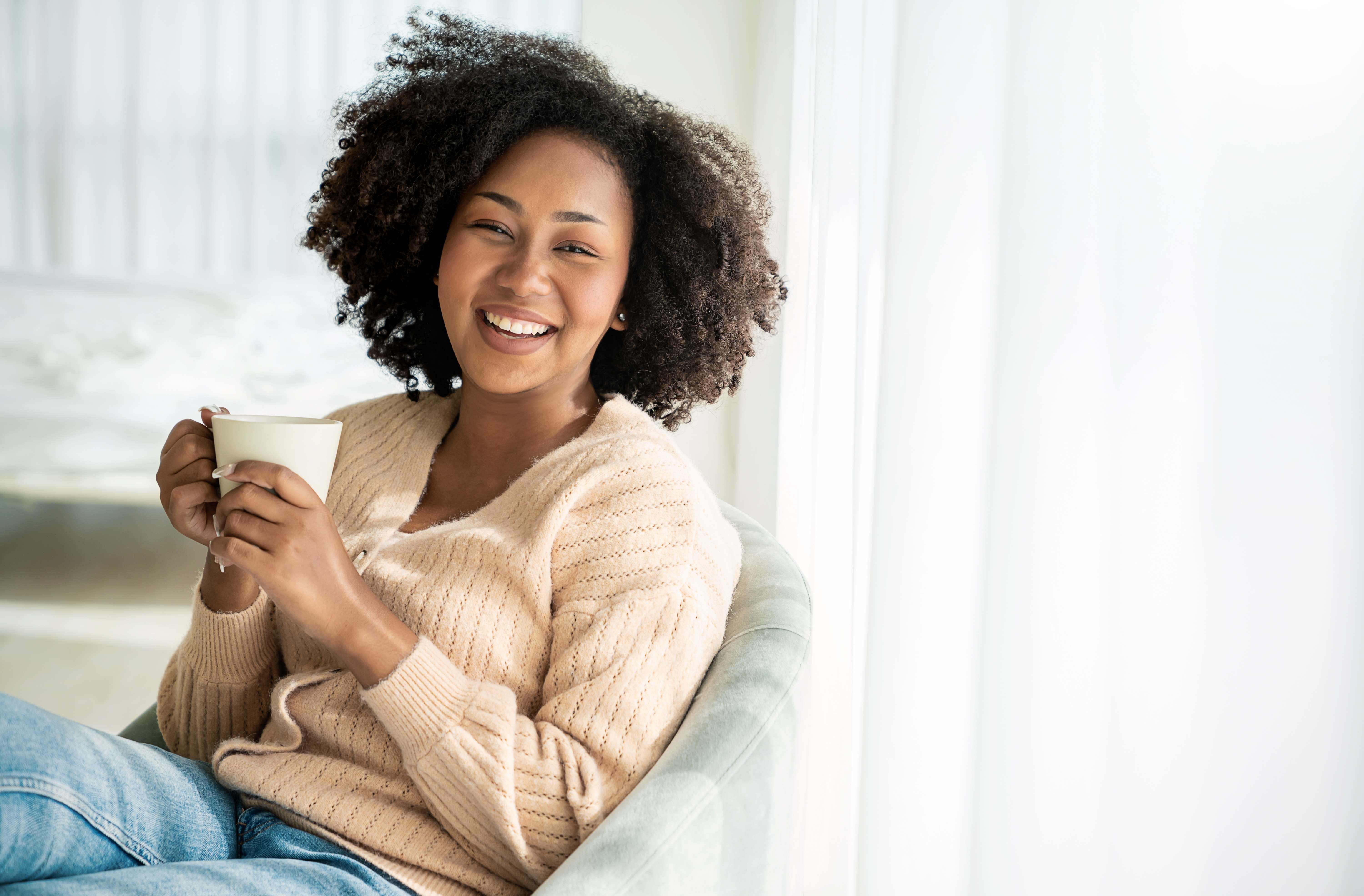 A happy woman enjoys a cup of hot coffee during a cozy morning at home.