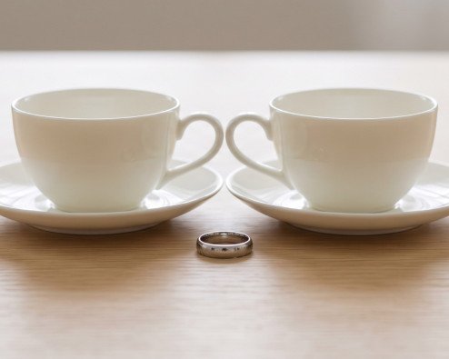 Two bone china cups and a platinum band on a pale wooden table for a 20 year anniversary gift