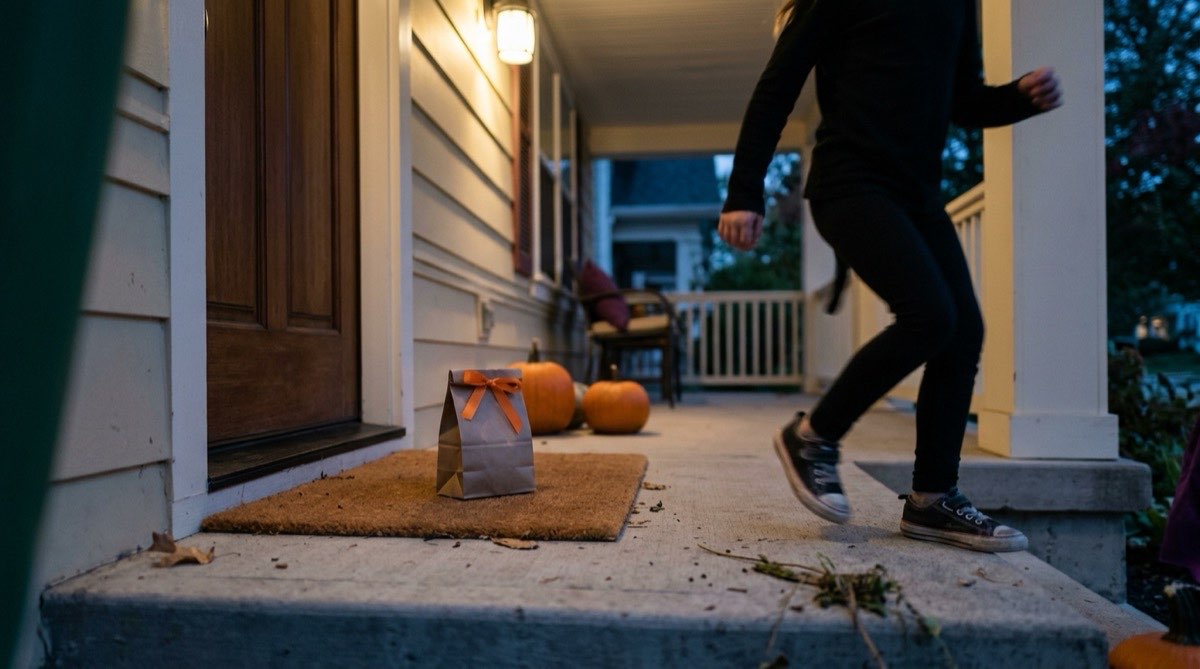 Paper treat bag with an orange ribbon left on a neighbor's doormat at dusk