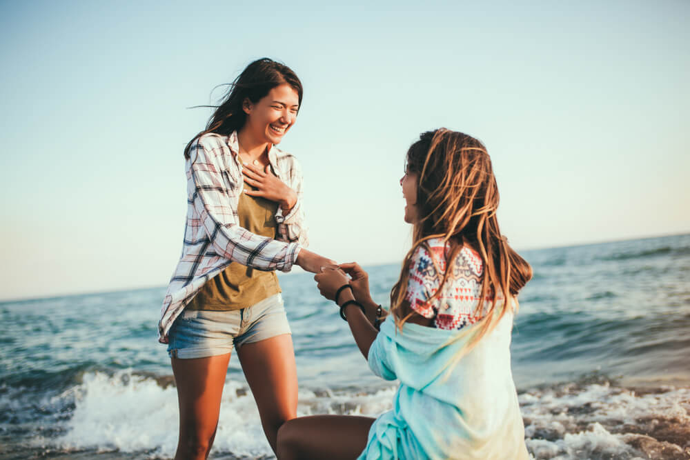A woman proposes to her girlfriend on the shore of a scenic beach.