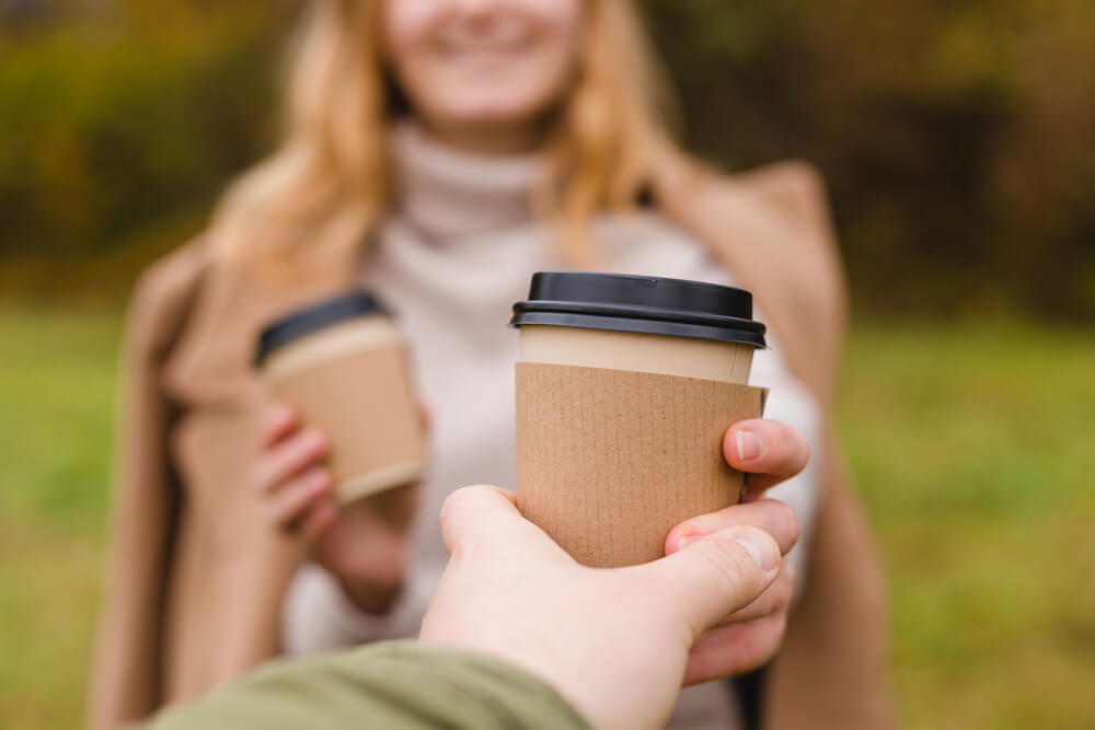 A woman brings her boyfriend a seasonal coffee drink on an autumn day. 