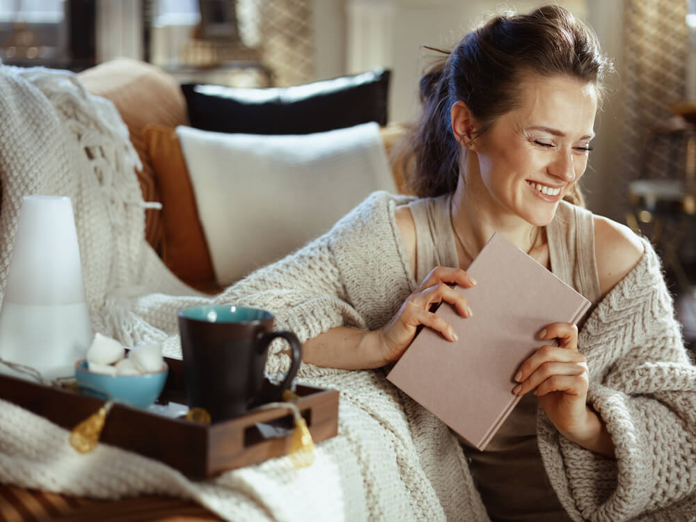 A woman gets cozy in a warm sweater at home on a fall day.