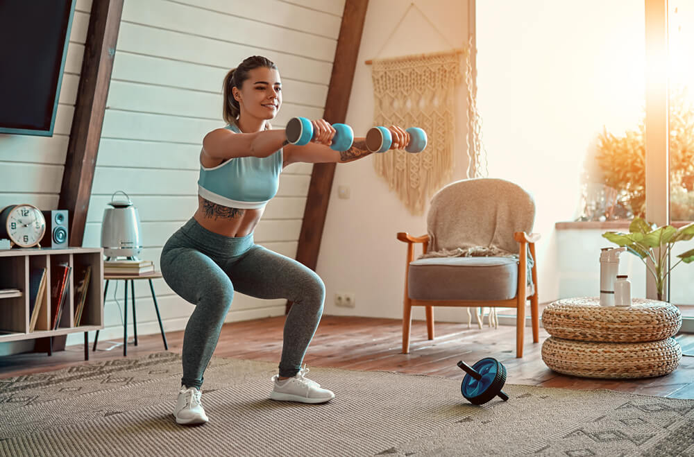A fit woman exercises with hand weights in her tidy home gym.