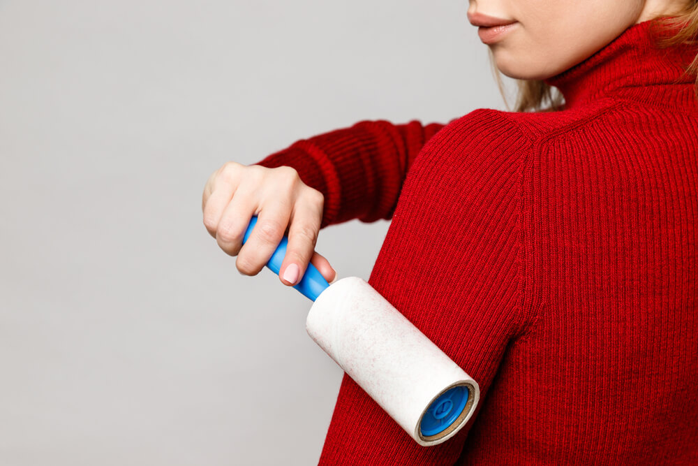 A woman cleans her sweater with a lint roller before going out on her birthday.