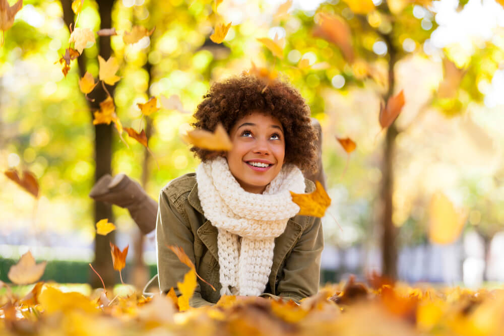 A woman enjoys fall weather by sitting outside and watching autumn leaves.