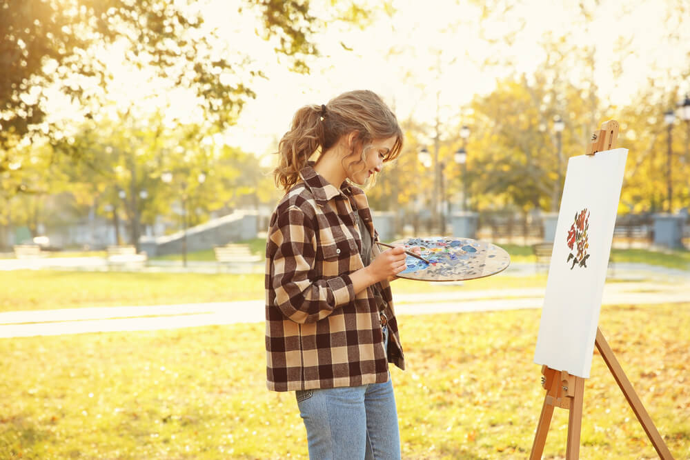 A woman paints a still life of autumn leaves outdoors.