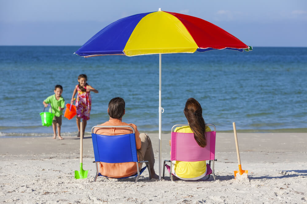 Parents spend their day at the beach under a shady umbrella while their kids play.