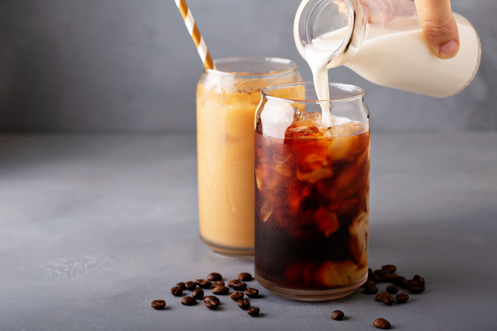 A milk alternative is poured into a glass of iced coffee.