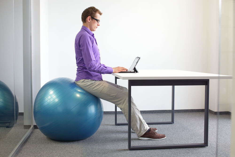 A working dad uses a ball chair to support his back at the office.