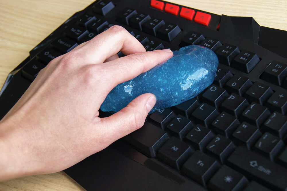 A man extracts the crumbs from his keyboard with cleaning slime.