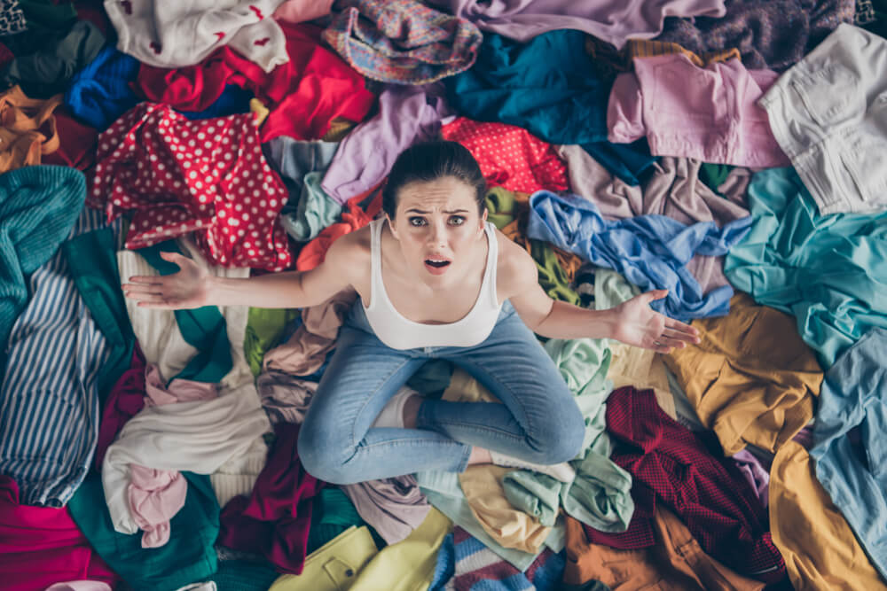 A disorganized woman is stressed out by the piles of laundry on her floor.