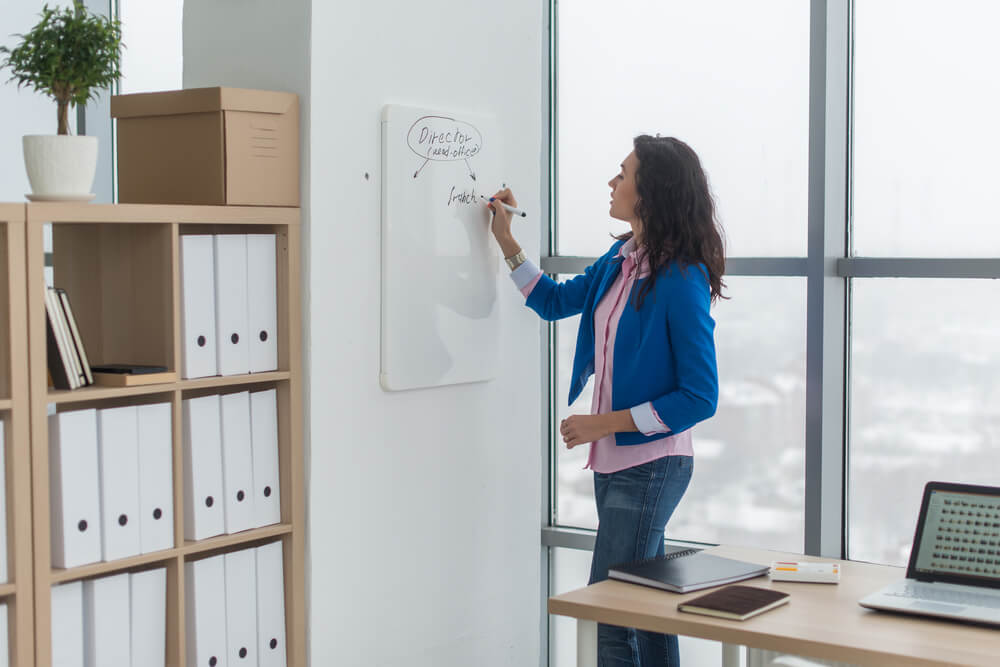 A businesswoman uses a dry erase board to stay organized in her office.