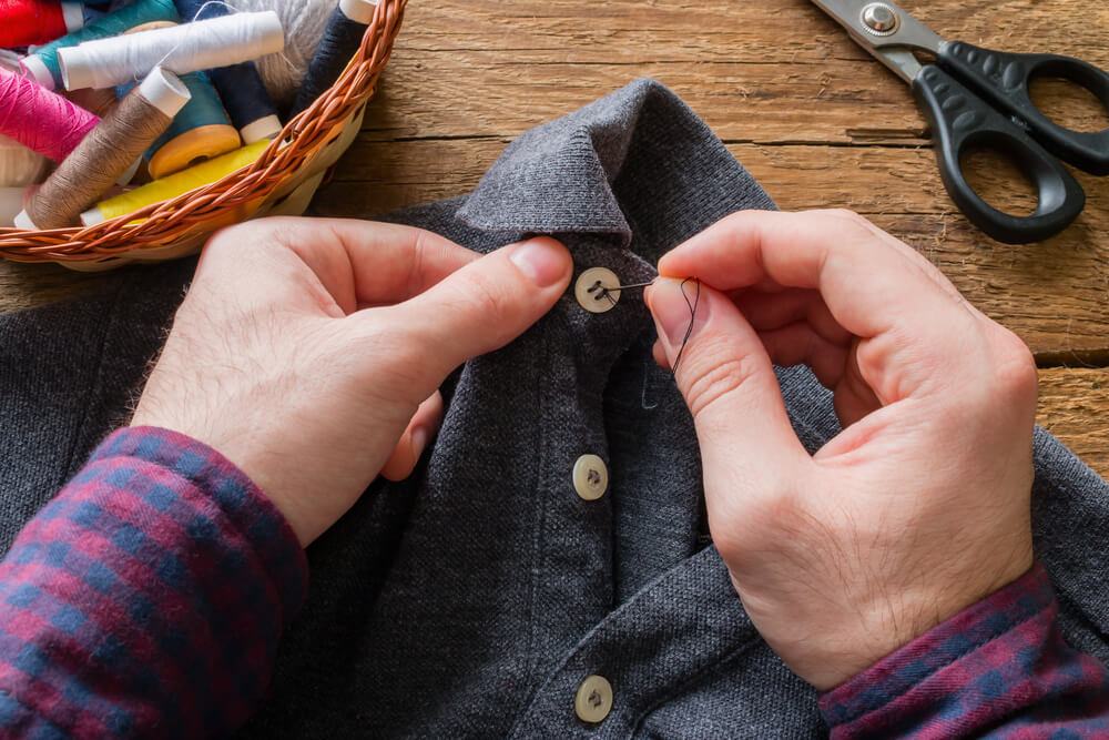 A resourceful man sews a button back onto his favorite shirt.