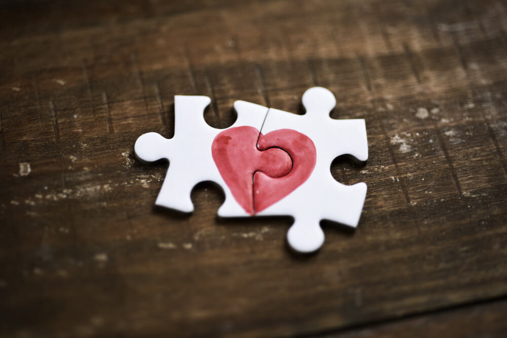 Two puzzle pieces come together to make a heart, symbolizing togetherness.