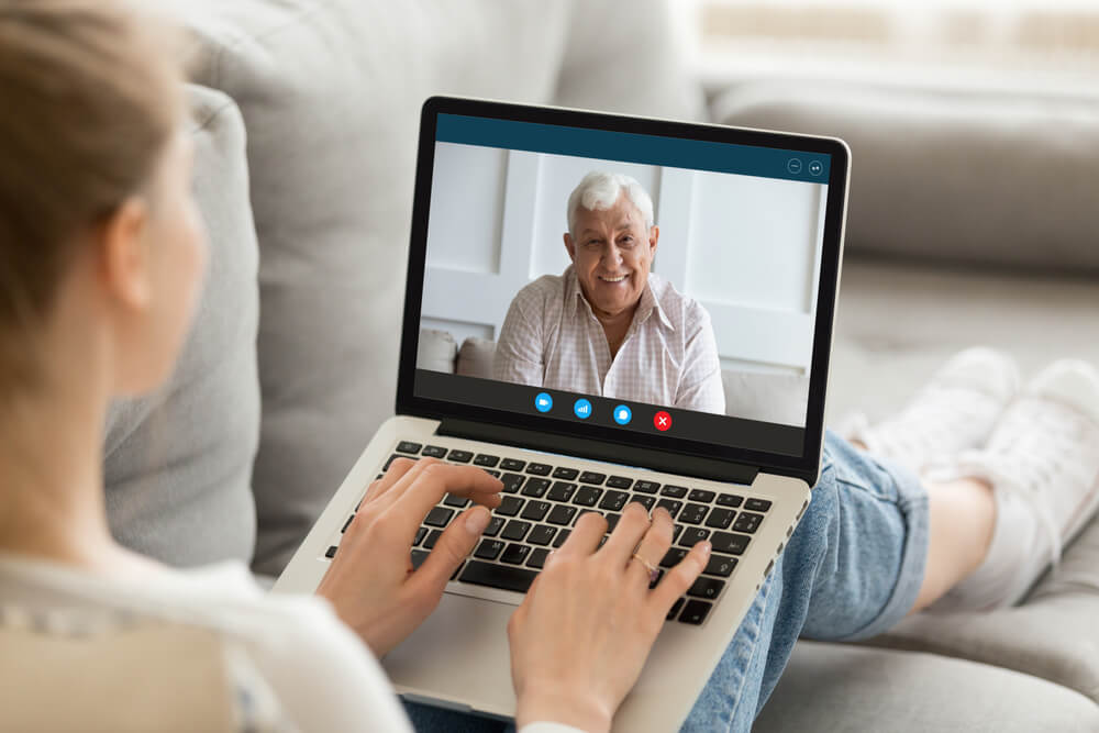 A young woman uses her laptop to have a virtual video call with her dad.