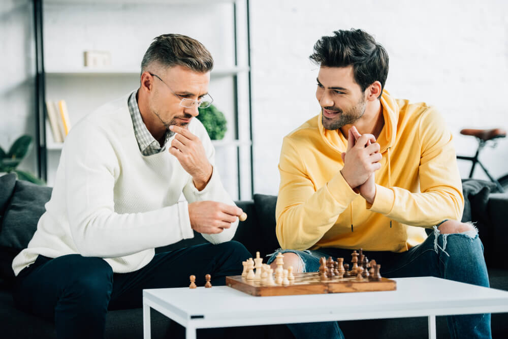 A single father plays a game of chess with his grown-up son.