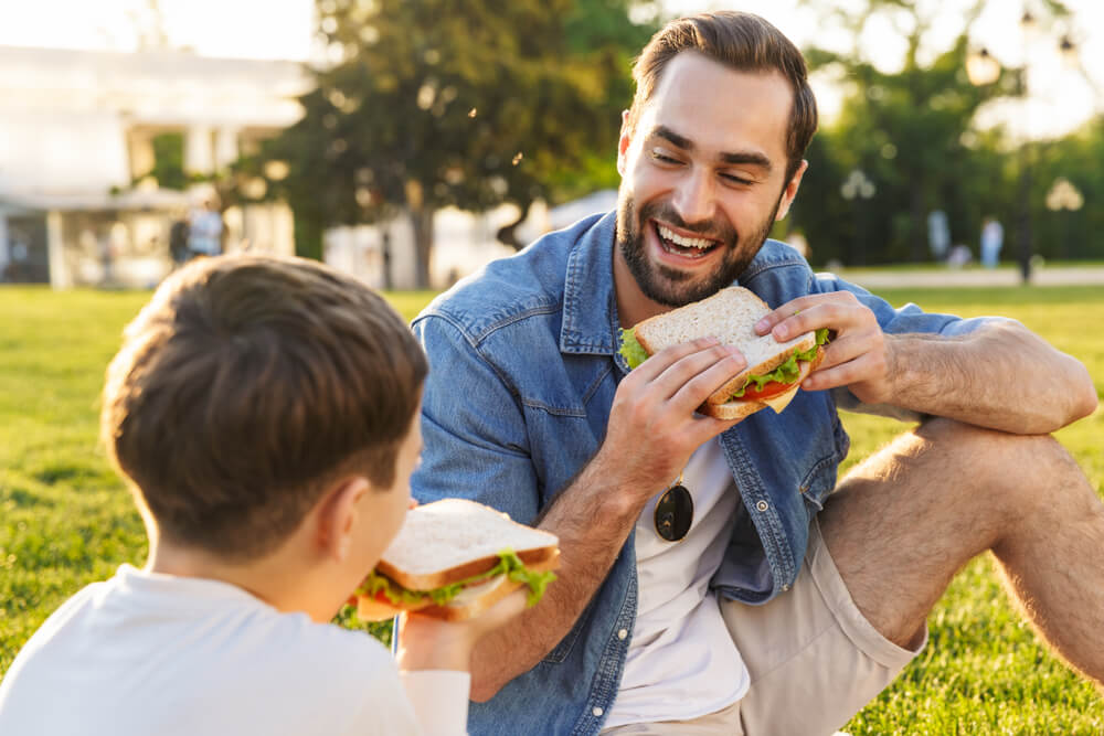 A single dad and his son enjoy a picnic together outdoors.