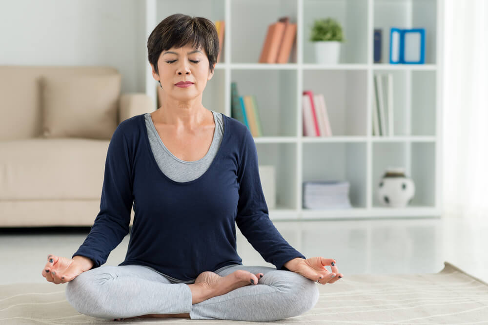 A calm older woman meditates in comfortable clothing.