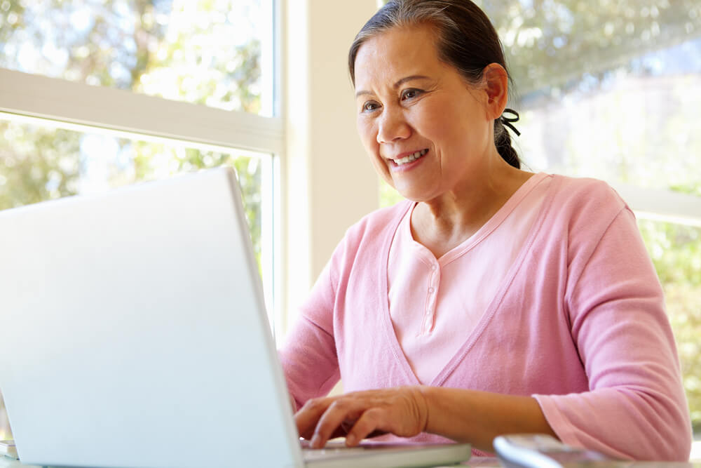 A retired senior woman attends virtual classes on her laptop.