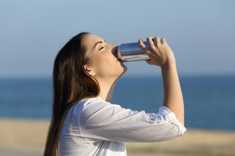 A woman relaxes at the beach with a delicious canned beverage.