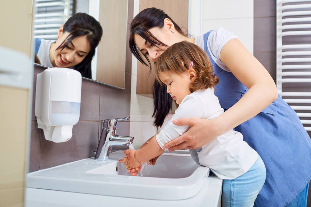 A single mom helps her daughter wash her hands with a touchless soap dispenser.