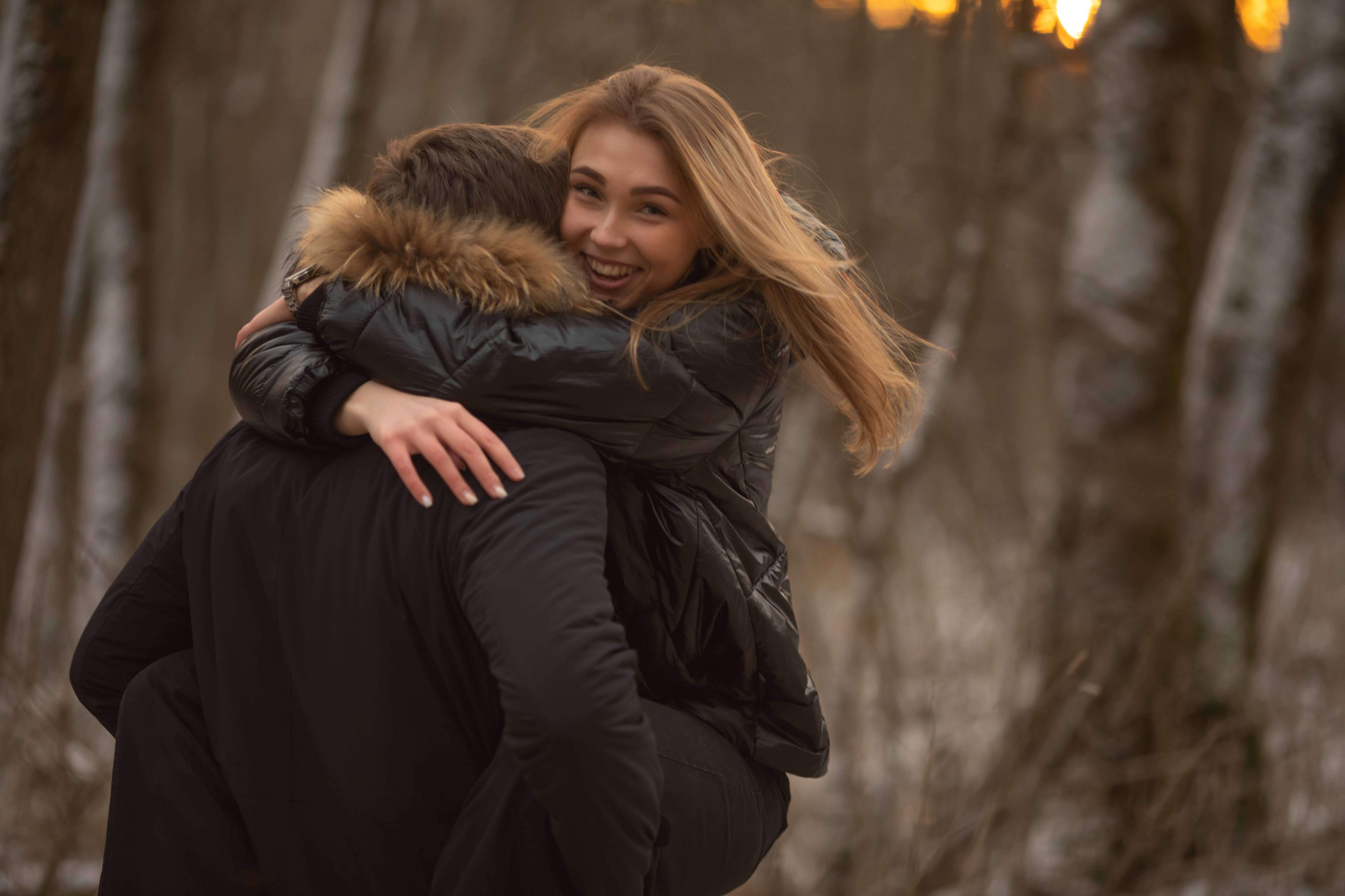 A smiling girlfriend in a warm winter jacket hugs her boyfriend on Valentine’s Day.