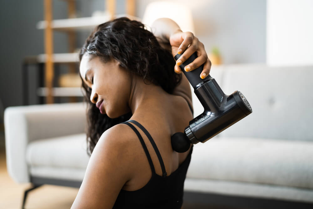 A woman eases the tension in her back with a massager during Scorpio season.