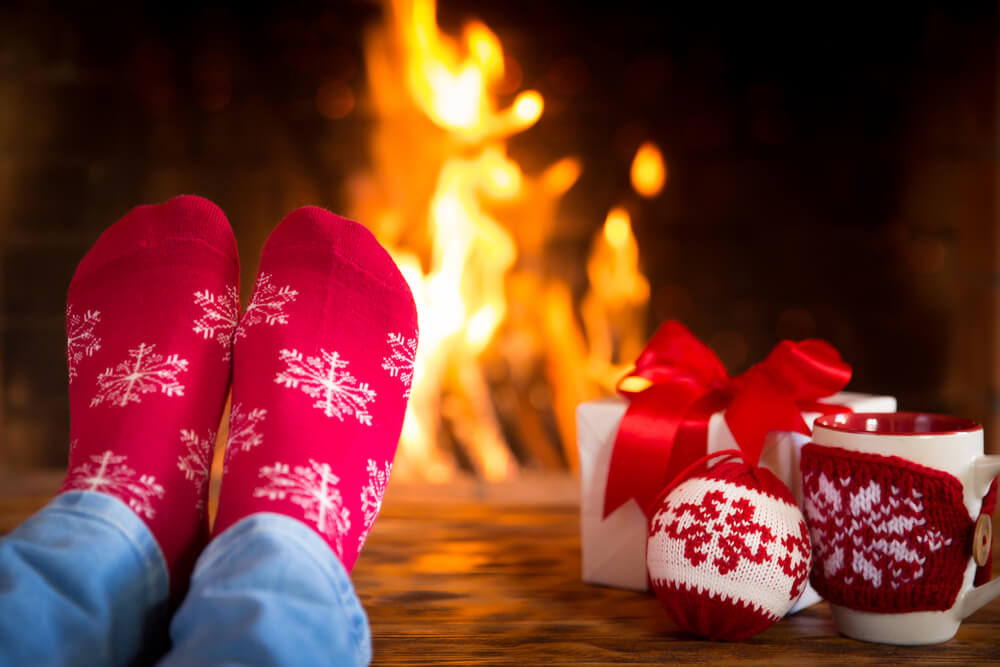 Woman at home. Feet in Christmas socks near fireplace