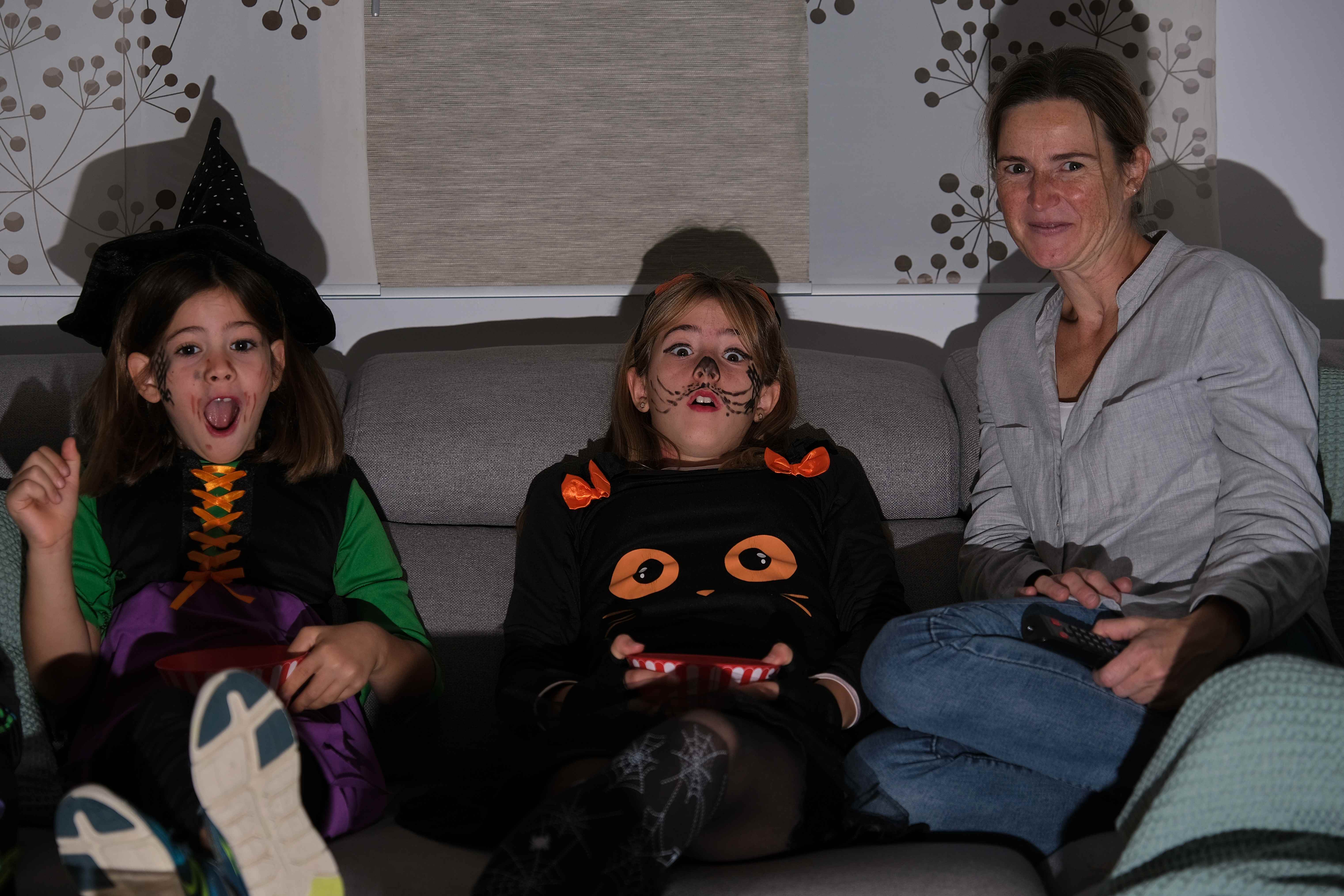 A mom and her daughters watch a family-friendly scary movie at home in October
