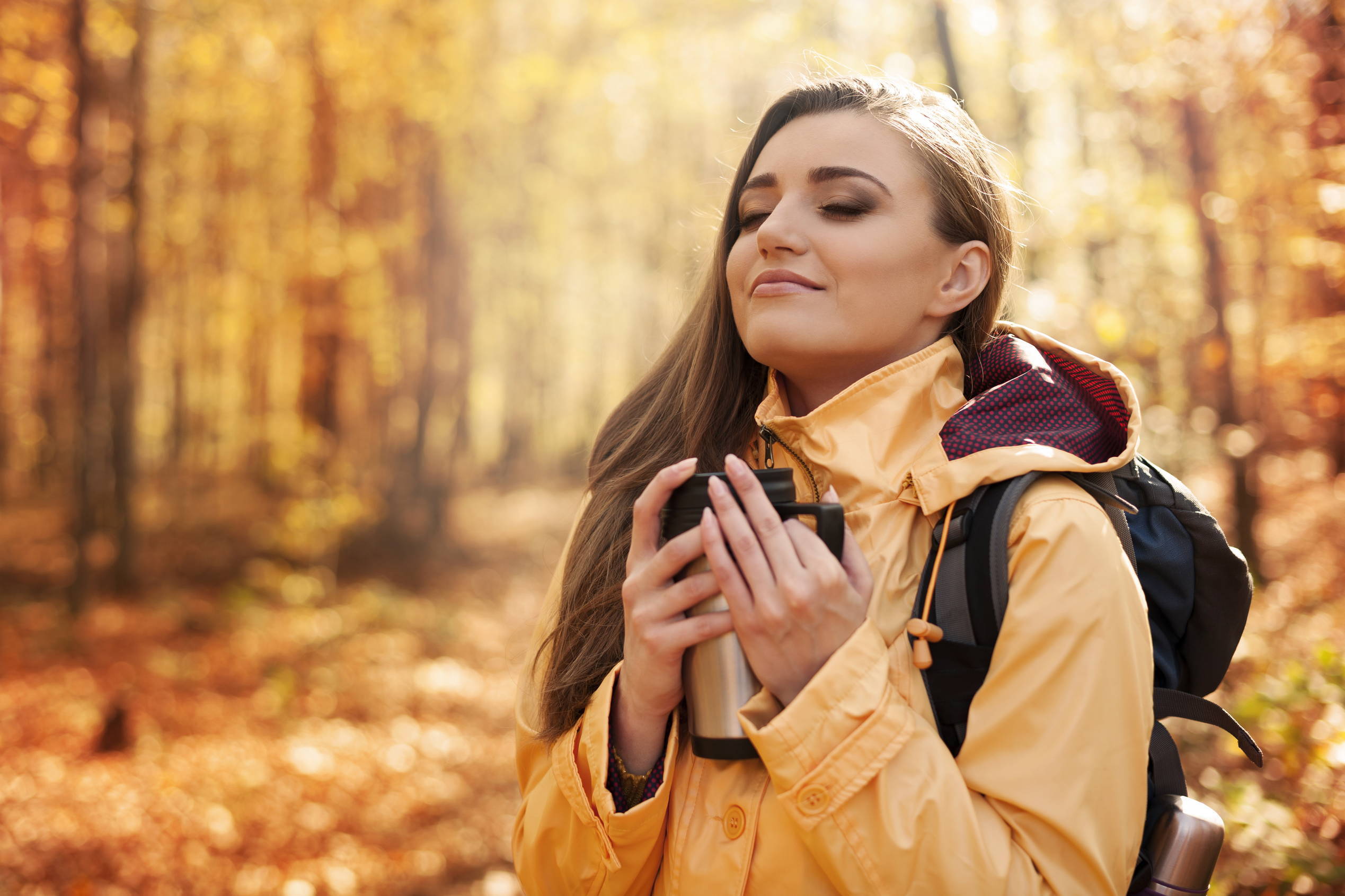 An adventurous woman enjoys coffee in a travel mug while hiking.