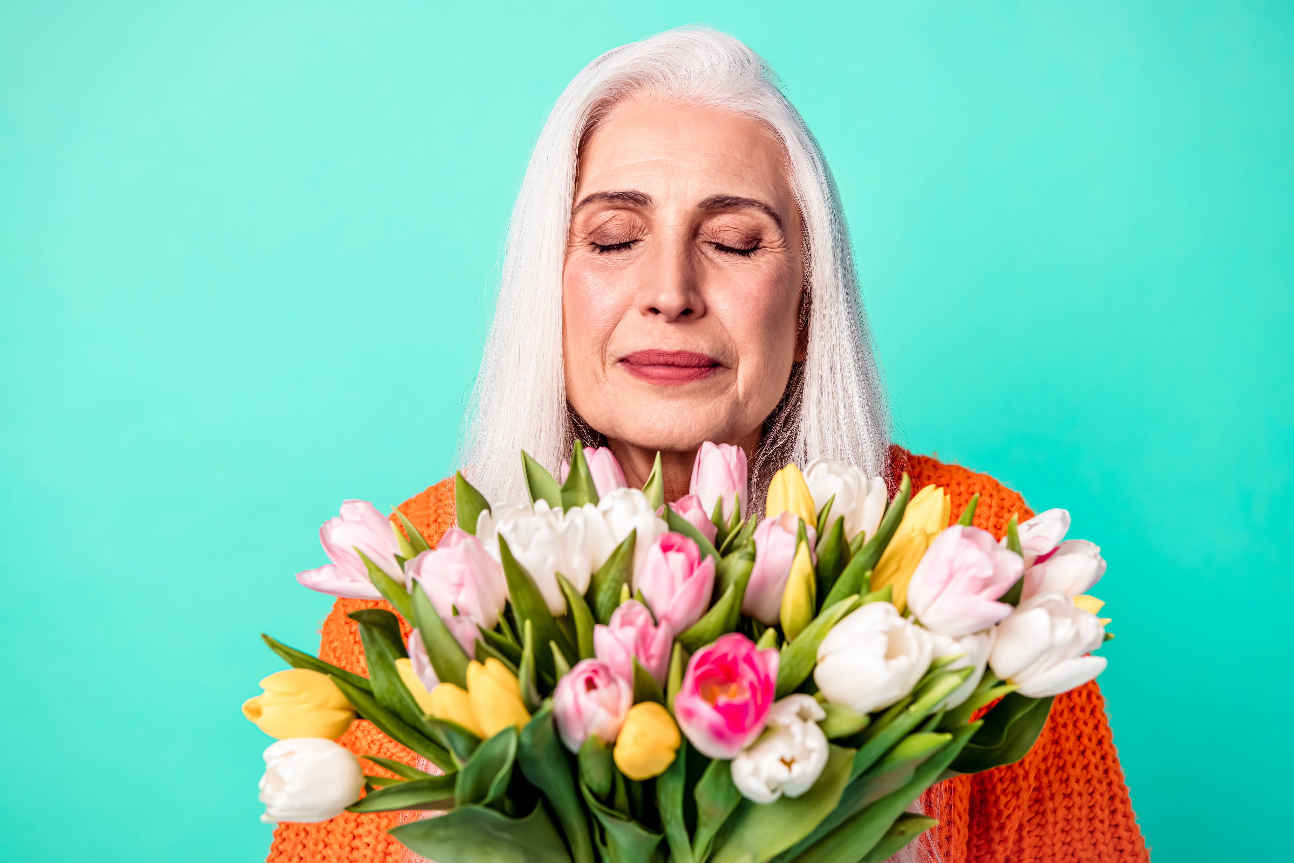 An older woman smells a beautiful bouquet sent by her grandchildren.