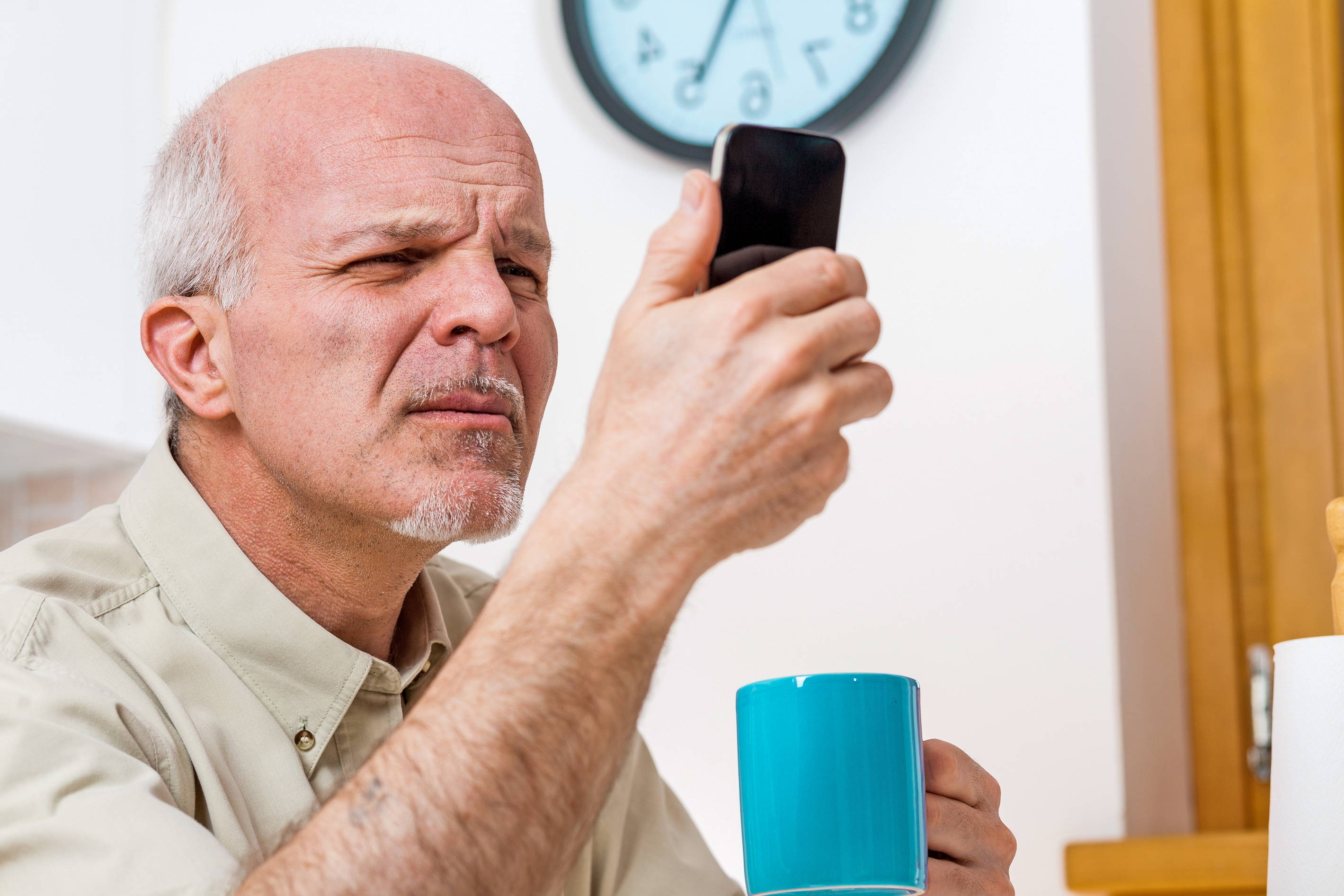 Grandpa struggles to read the small text on his smartphone. 