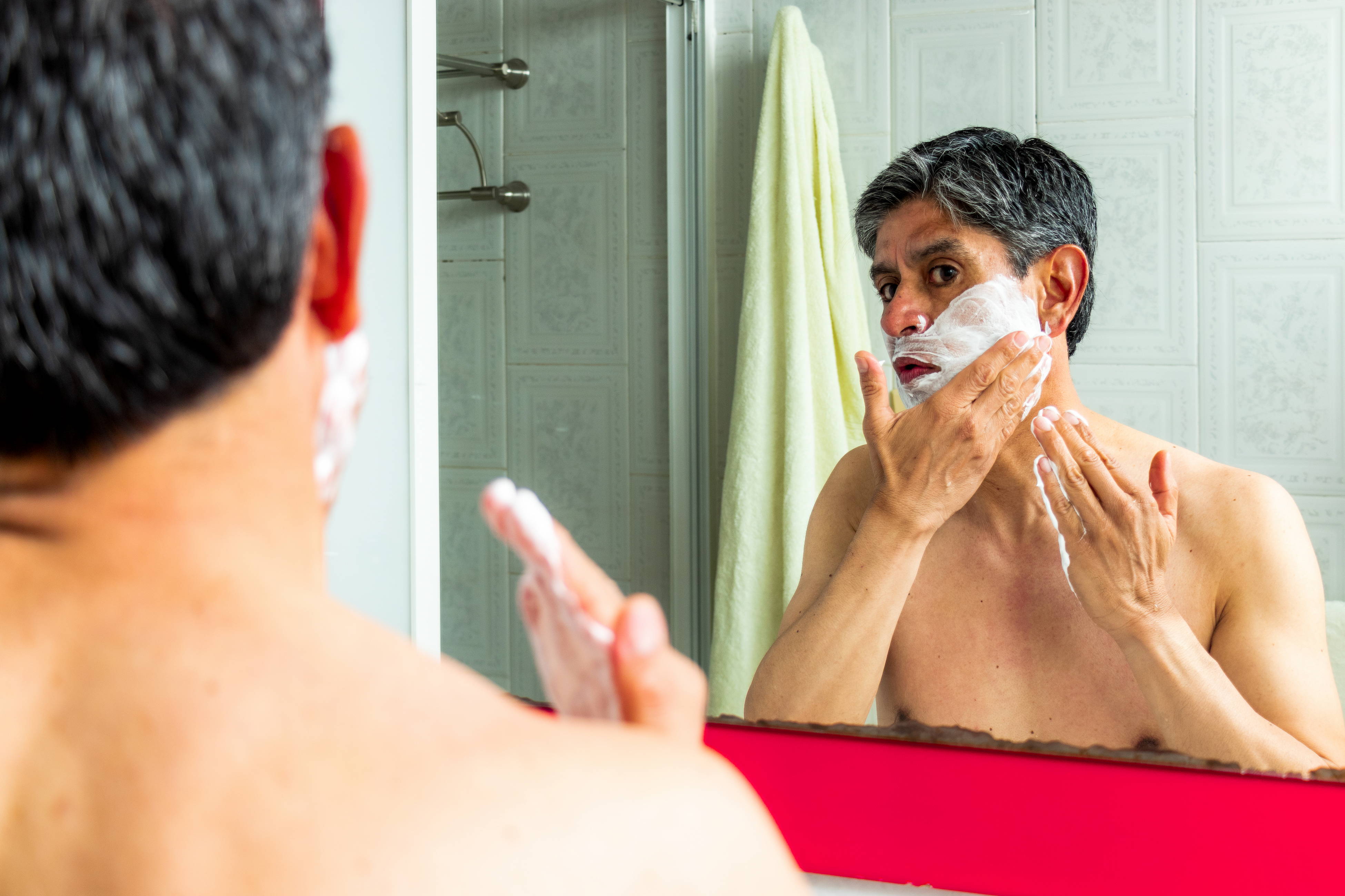 A man tries out his new shaving kit in front of the bathroom mirror.
