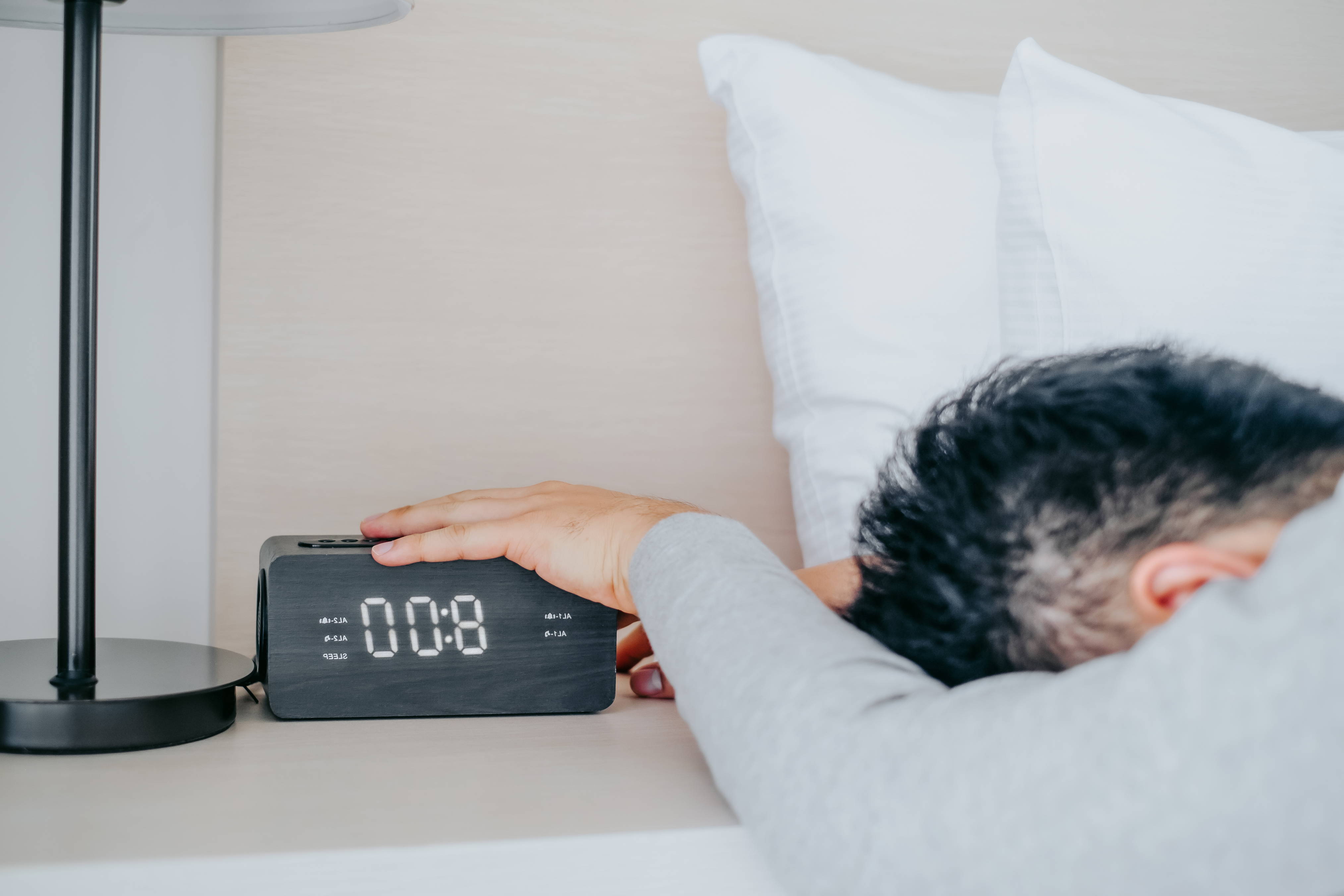 A young man hits the snooze button on his alarm clock in the morning.