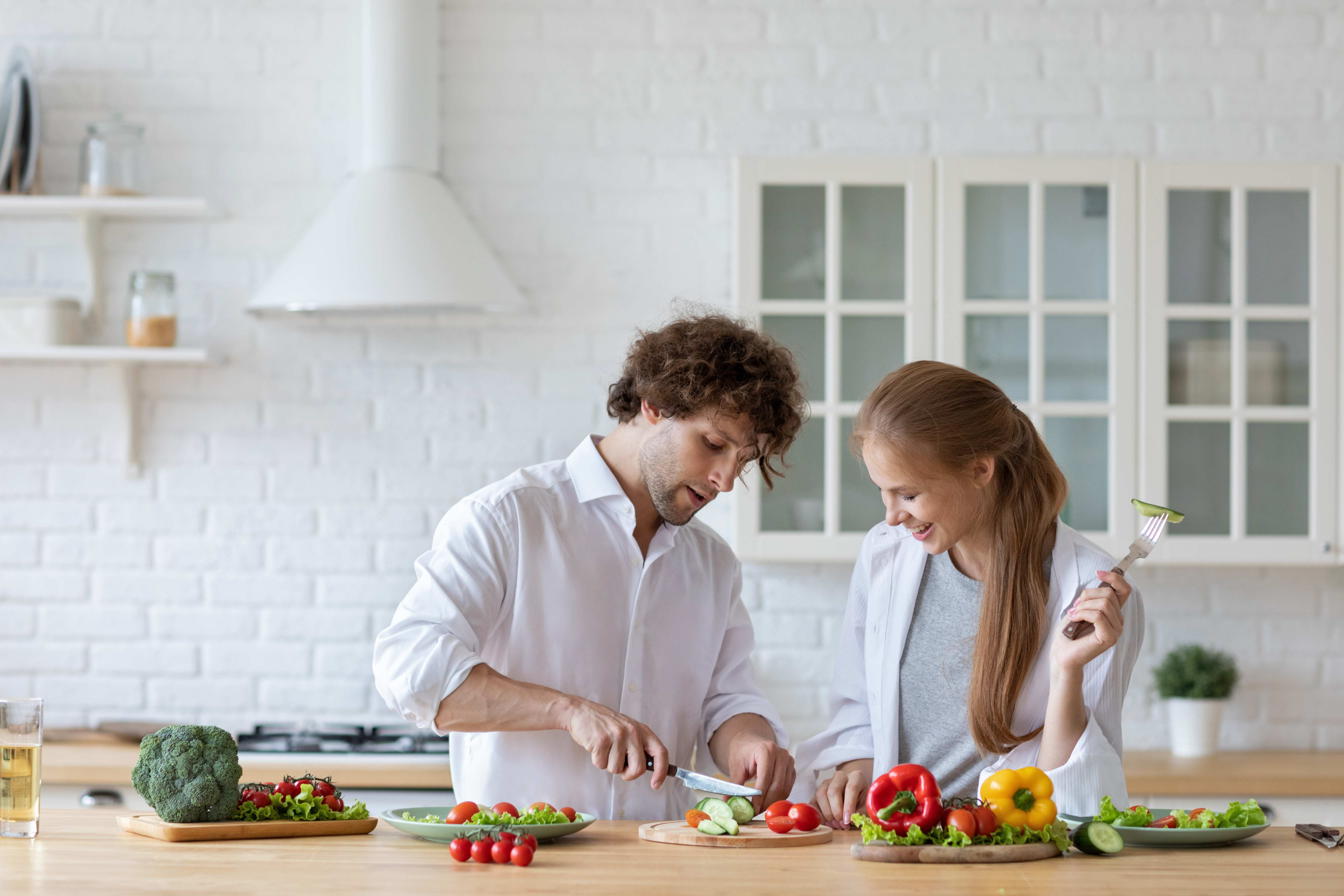 A happy couple stays healthy by cooking a meal at home with fresh ingredients.