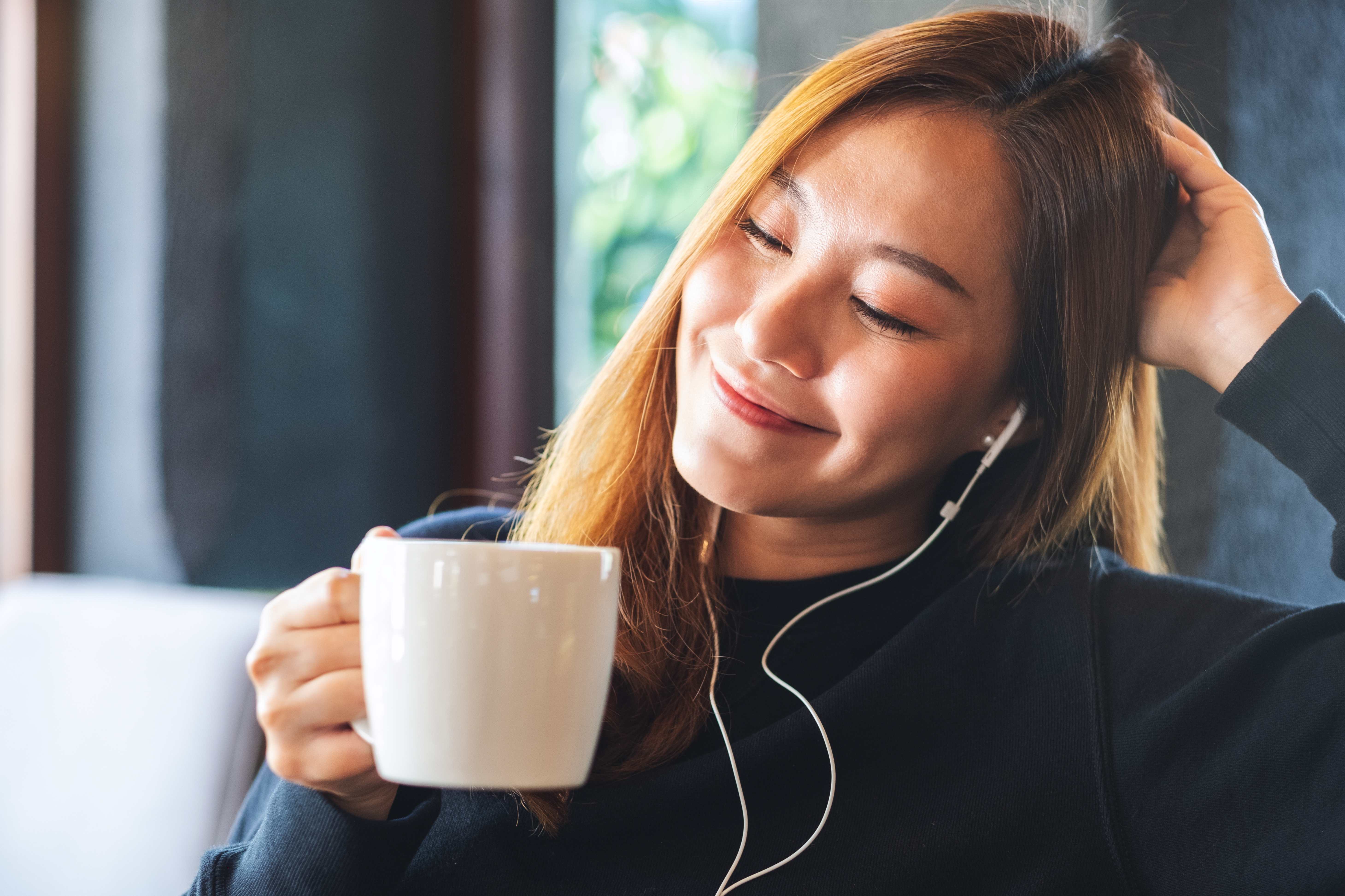 A woman practices self-care with a cup of tea and relaxing music. 