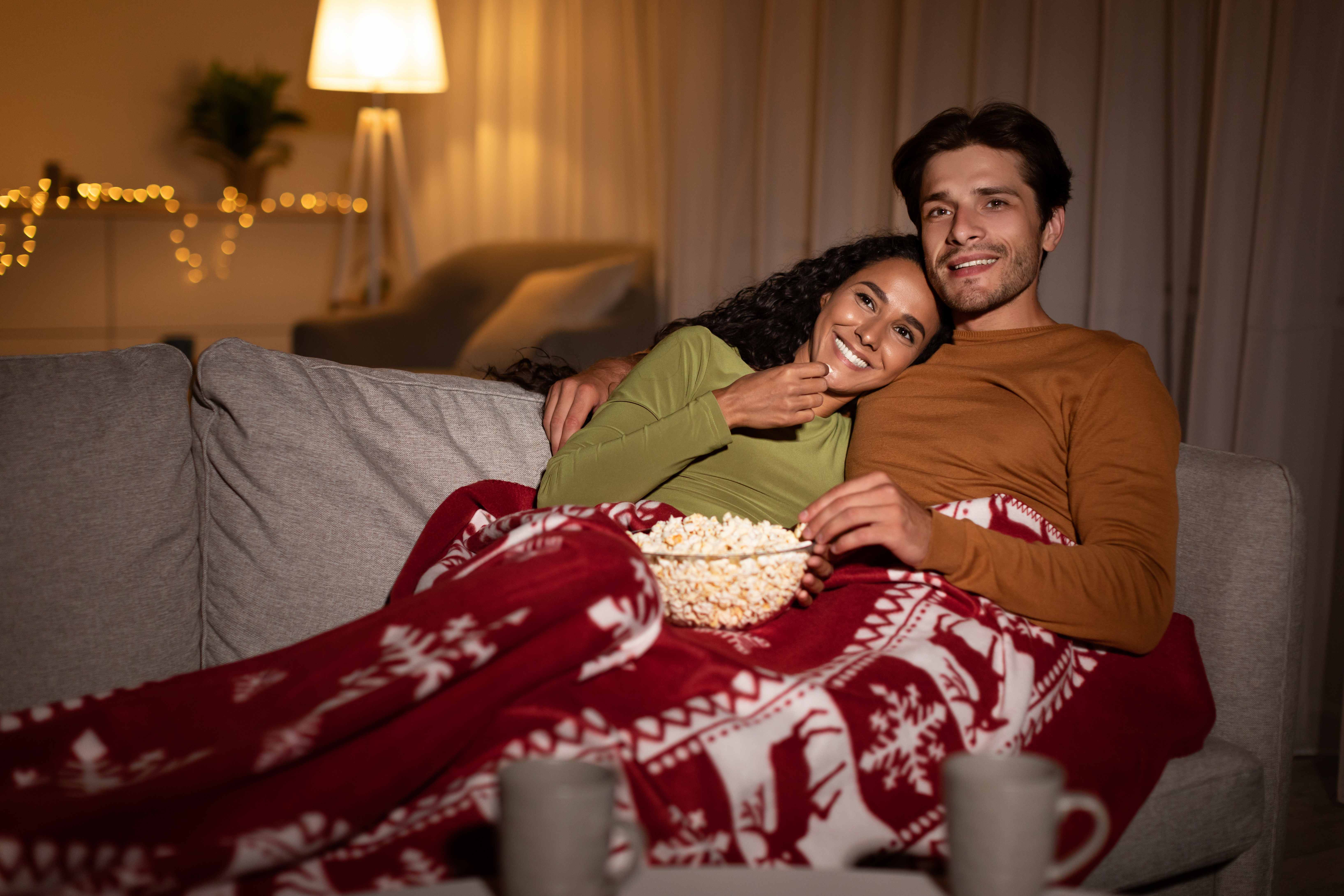 A man enjoys a cozy date night at home on the couch with his girlfriend. 
