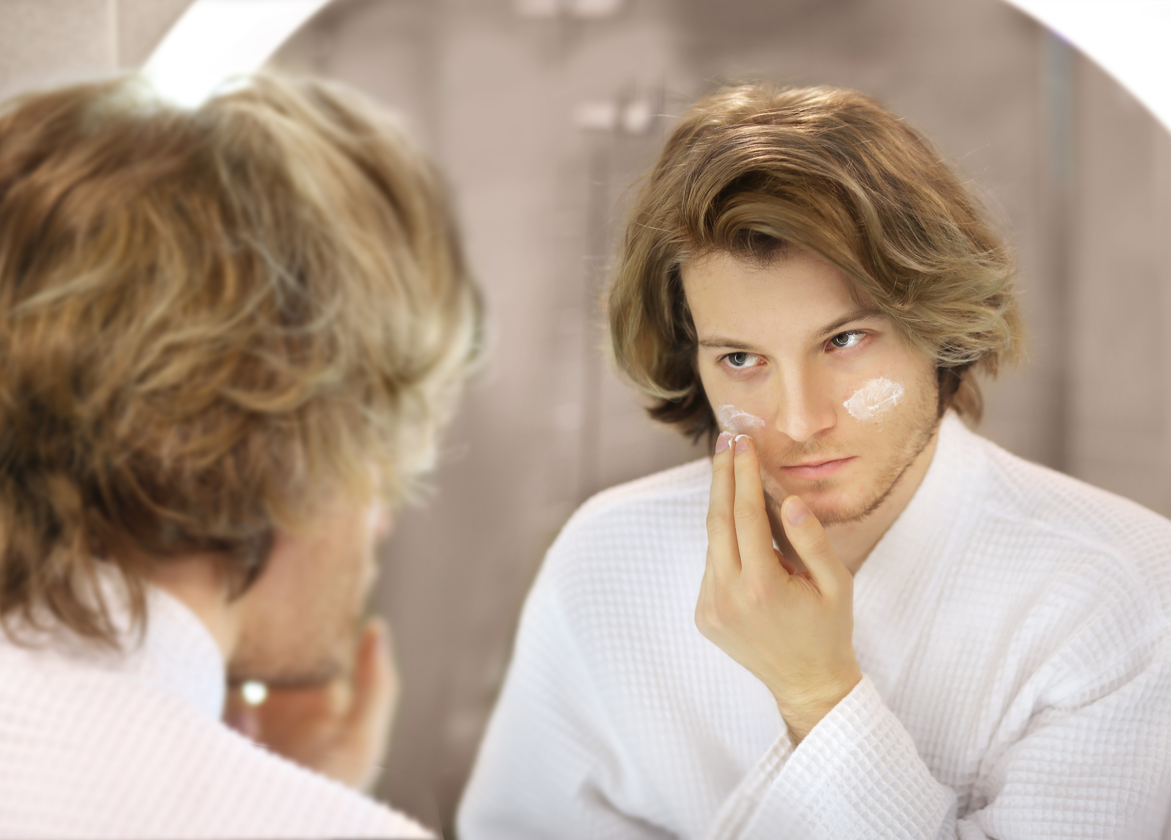 A man practices self-care by applying cream under his eyes. 