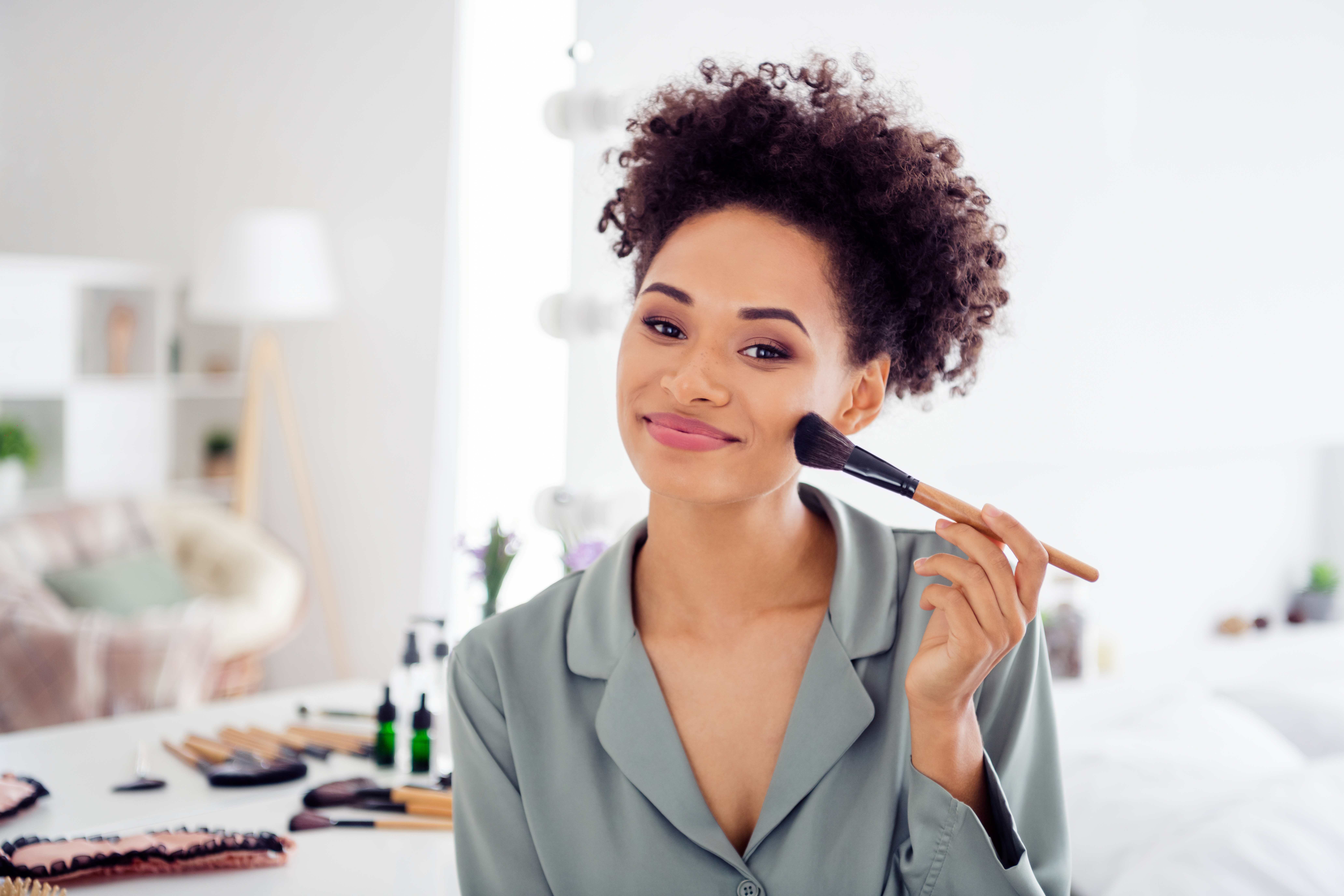 A woman applies blush with a makeup brush to get ready for her date.