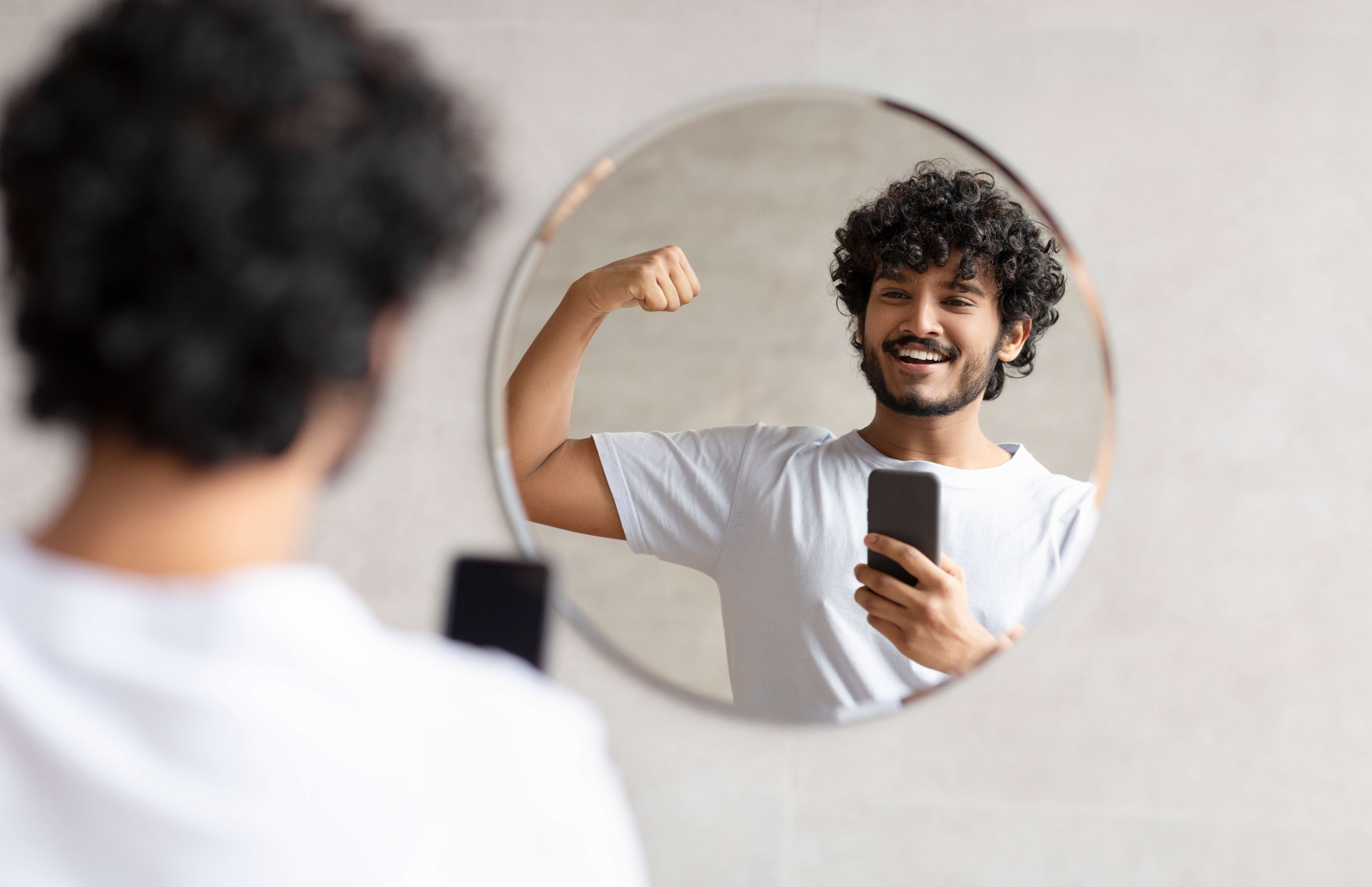A man boosts his self-confidence by taking a selfie in the mirror. 