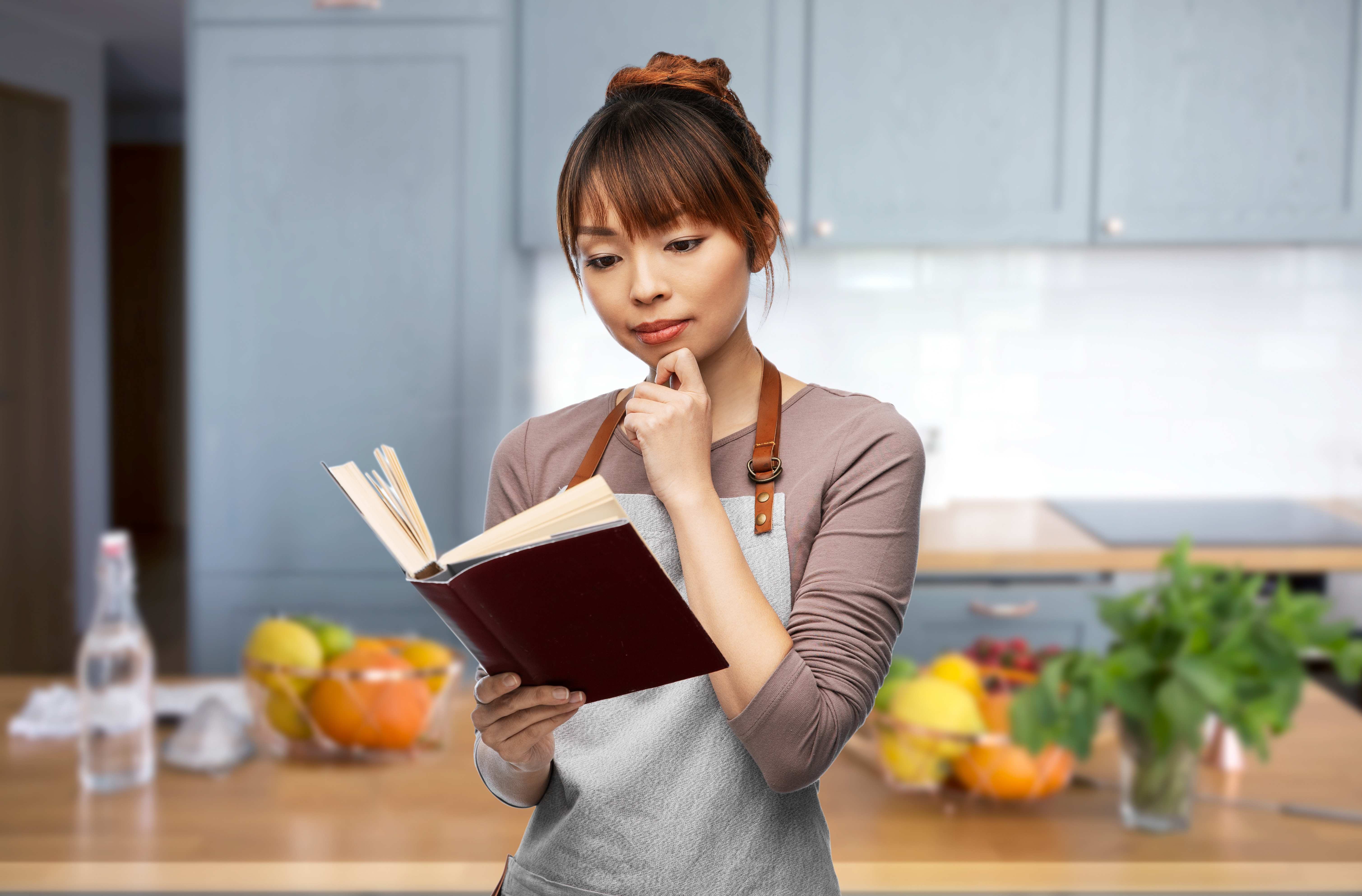 A vegetarian woman cooks herself a healthy meal from a plant-based cookbook.