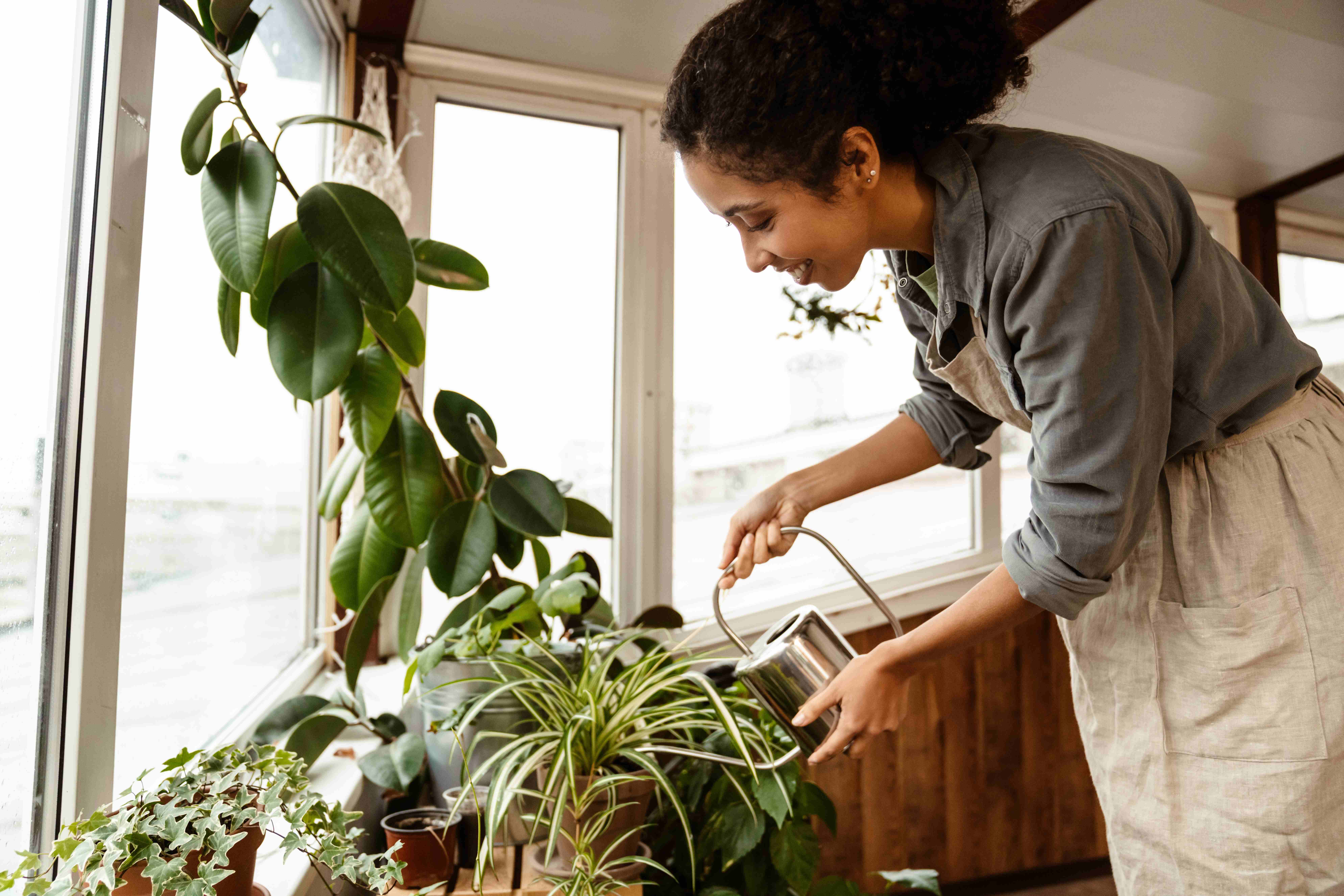 A sensitive Pisces woman waters her potted plants indoors. 
