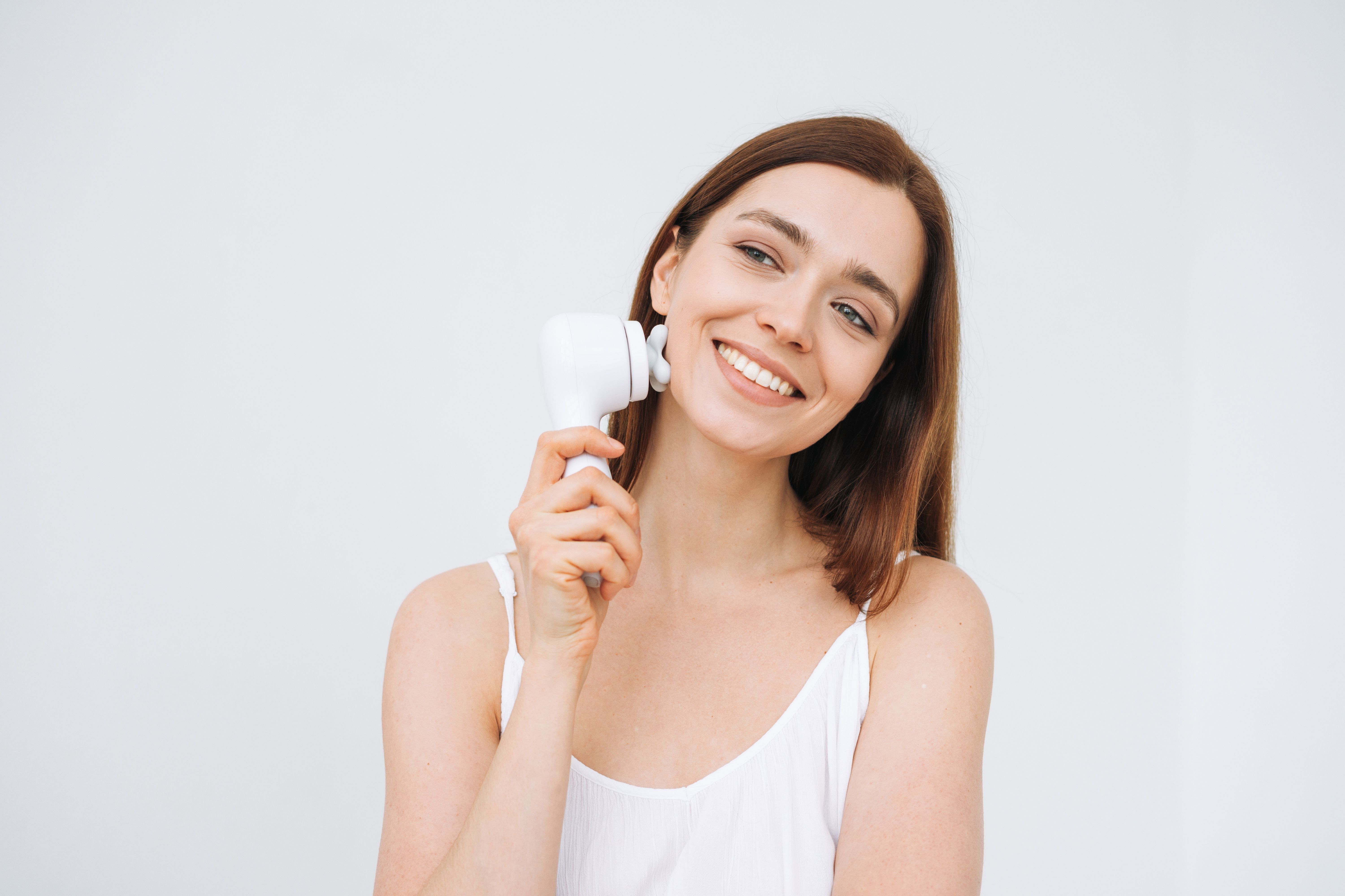 A relaxed woman uses an electric face massager in her skin care routine. 