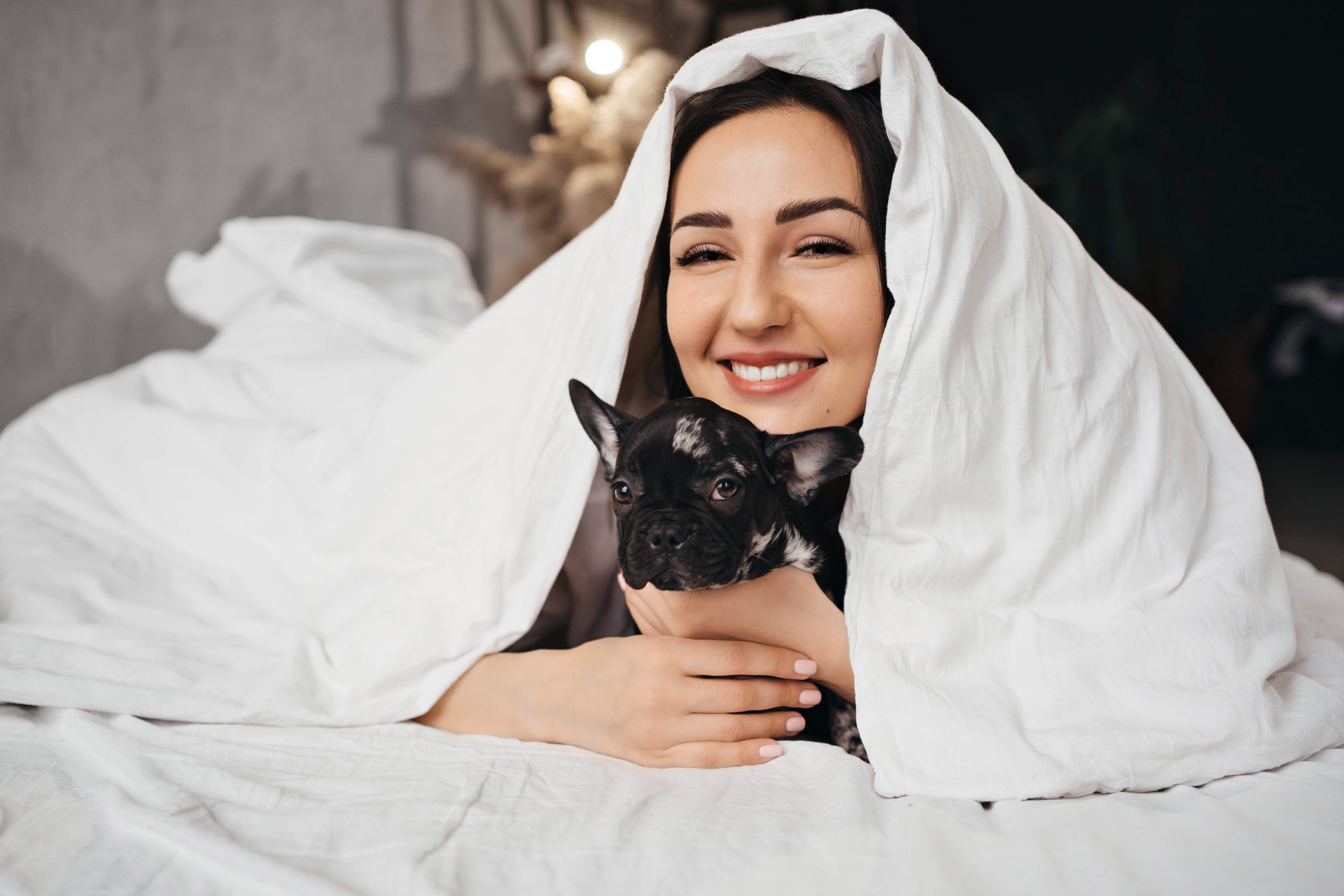 A woman relieves stress by cuddling her dog underneath a weighted blanket.