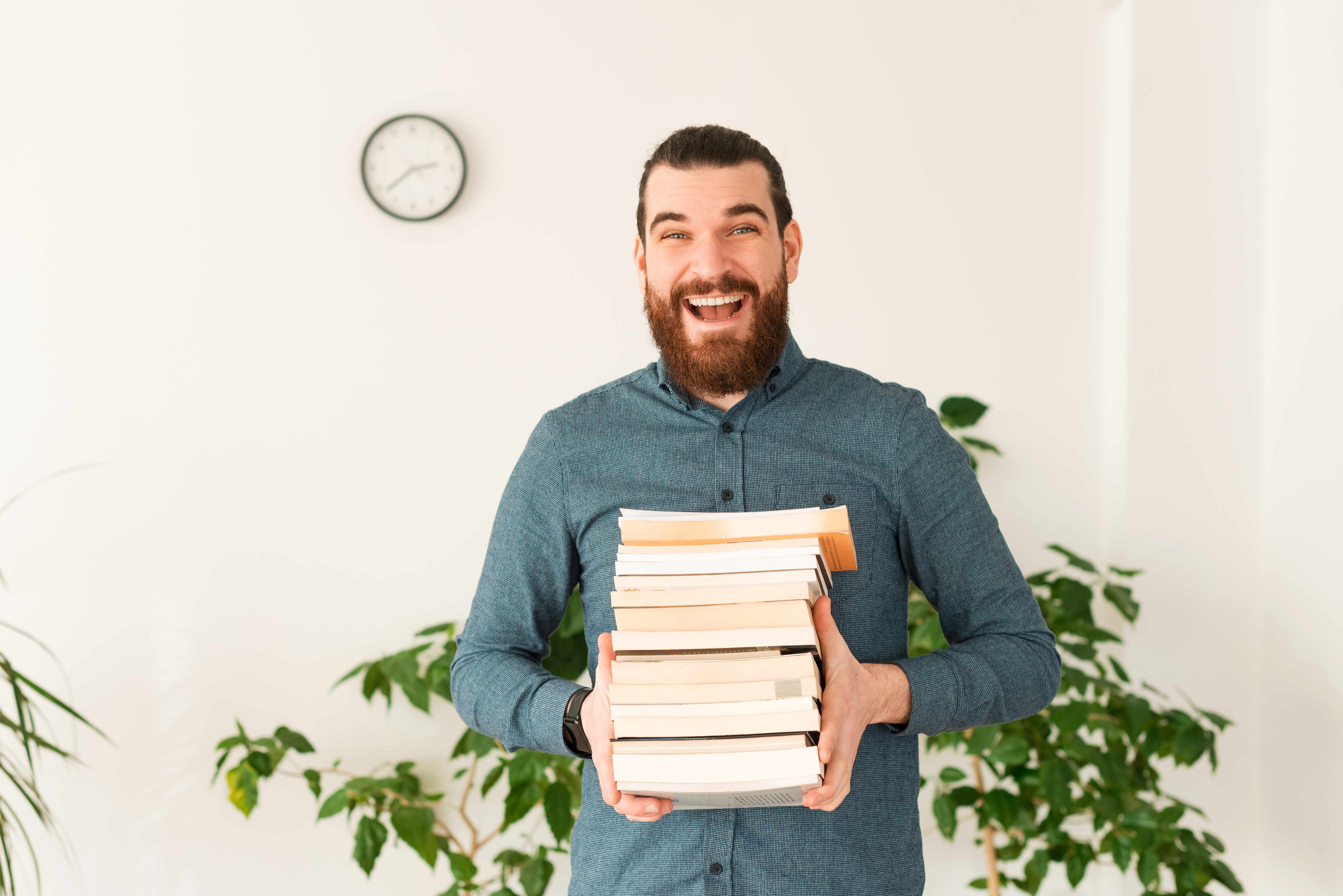 A man is excited to start reading the stack of books in his arms.