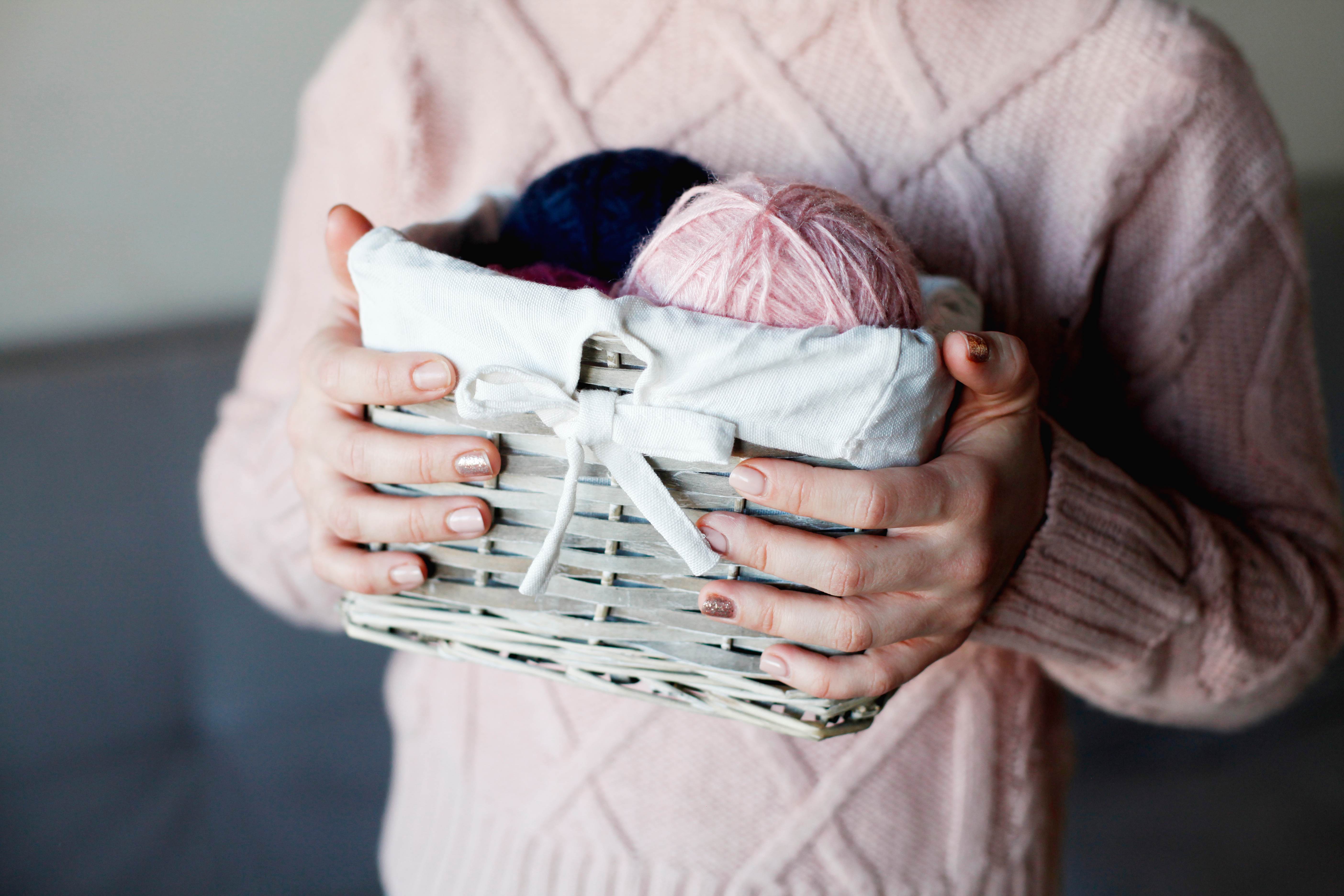 A woman holds a basket full of colorful balls of yarn for knitting.