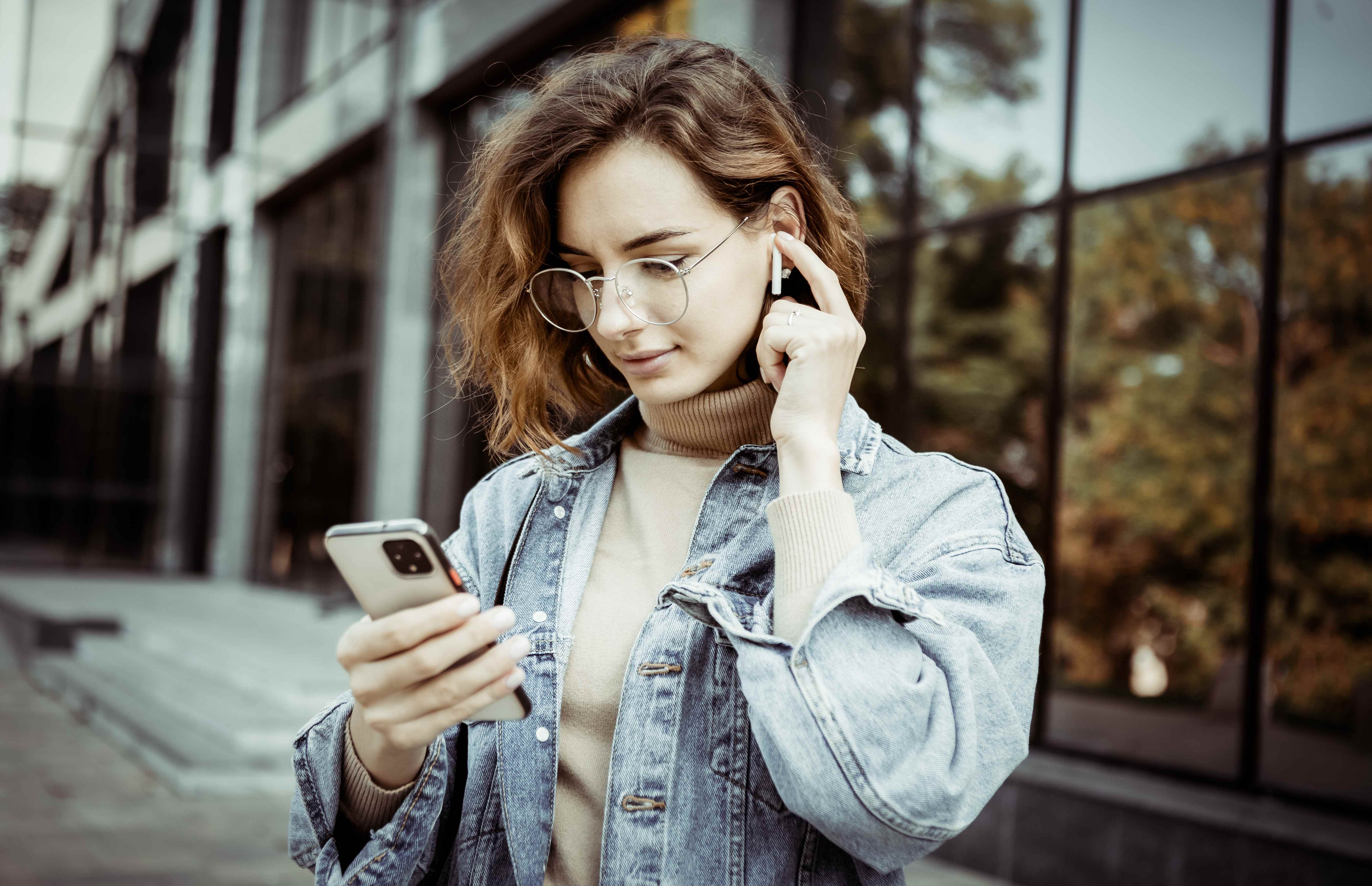 A young mom uses wireless earbuds to listen to a podcast while running errands.